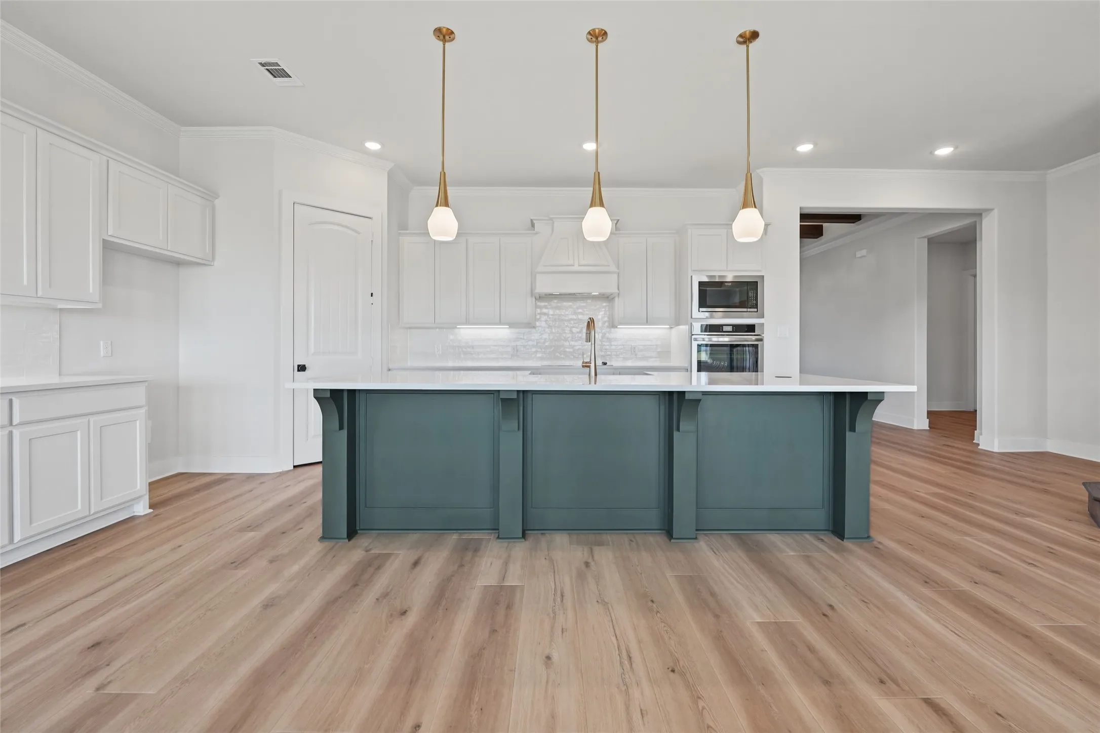 Spacious kitchen featuring white cabinetry, a large island with a contrasting finish, stainless steel appliances, and wood-finish flooring
