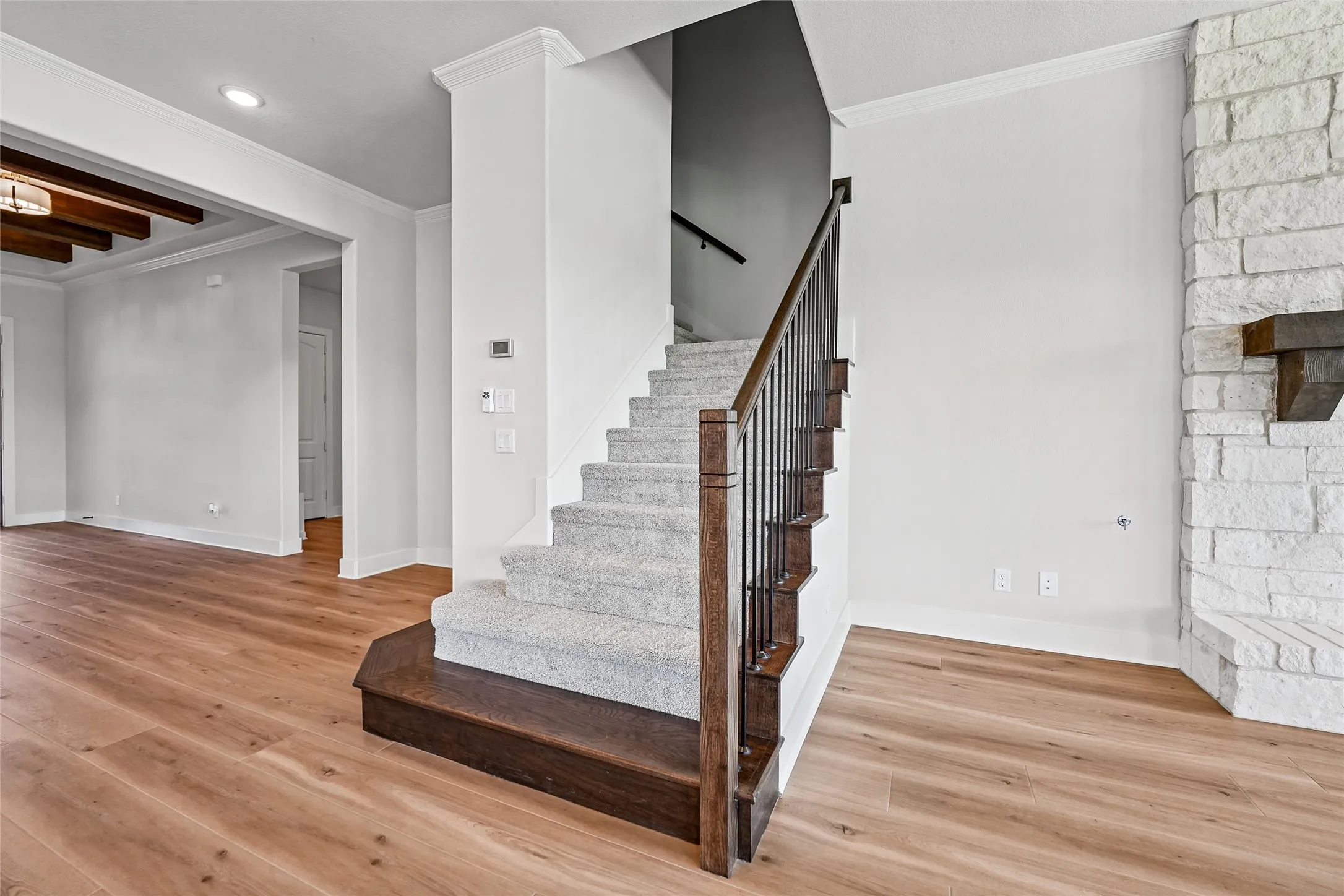 Hardwood-finish flooring, carpeted staircase with dark wood newel posts and iron balusters, stone fireplace with wood mantel, and crown molding