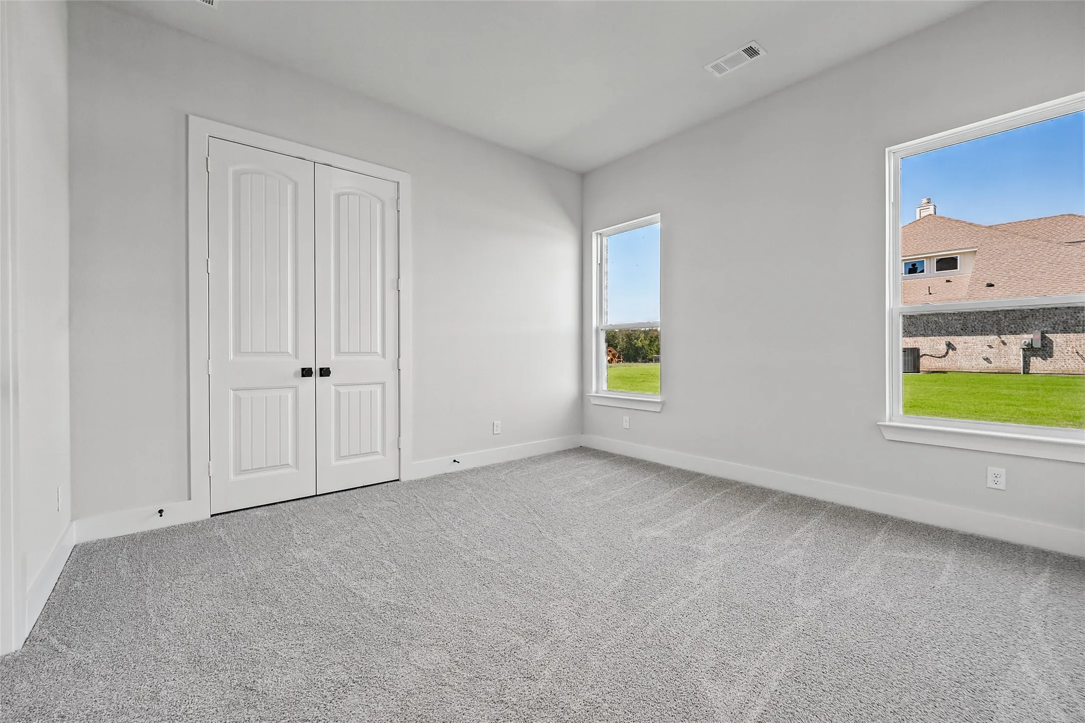 Light gray wall paint, gray patterned carpet, white trim, two white windows, and white double doors
