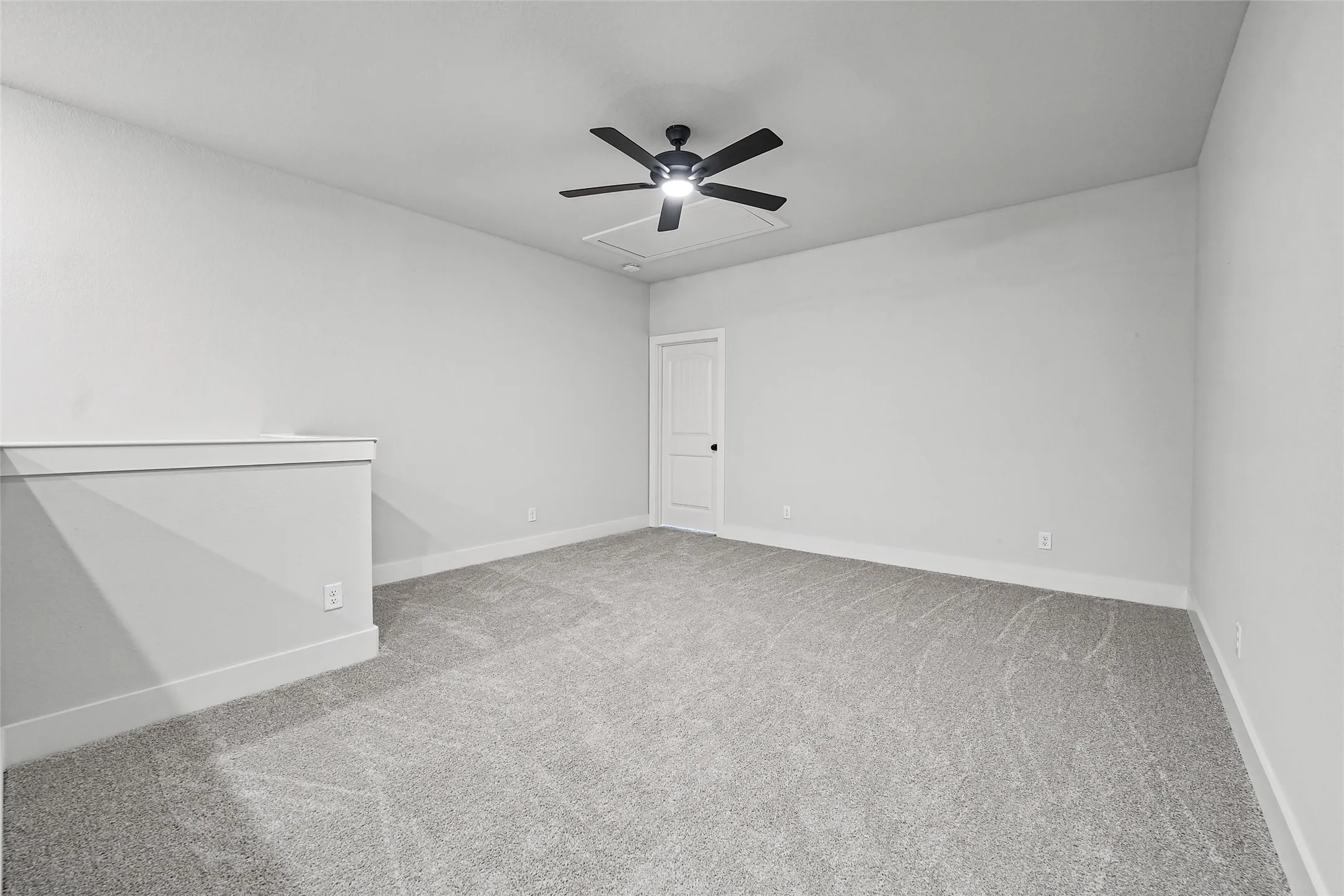 Carpeted loft space with a modern ceiling fan, white paneled door, and a half-wall balustrade