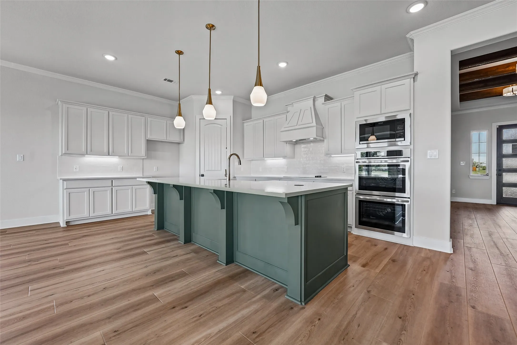Wood-finish flooring, white cabinetry, a teal island with a white countertop, and stainless steel built-in double ovens