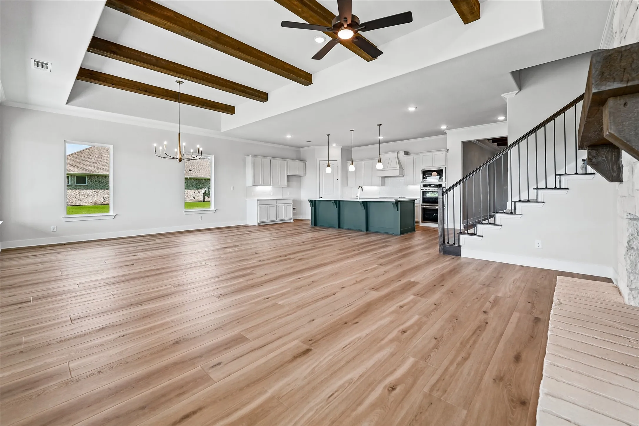 Open-concept living space with wood-finish flooring, exposed ceiling beams, a built-in kitchen island, and a staircase featuring metal balusters