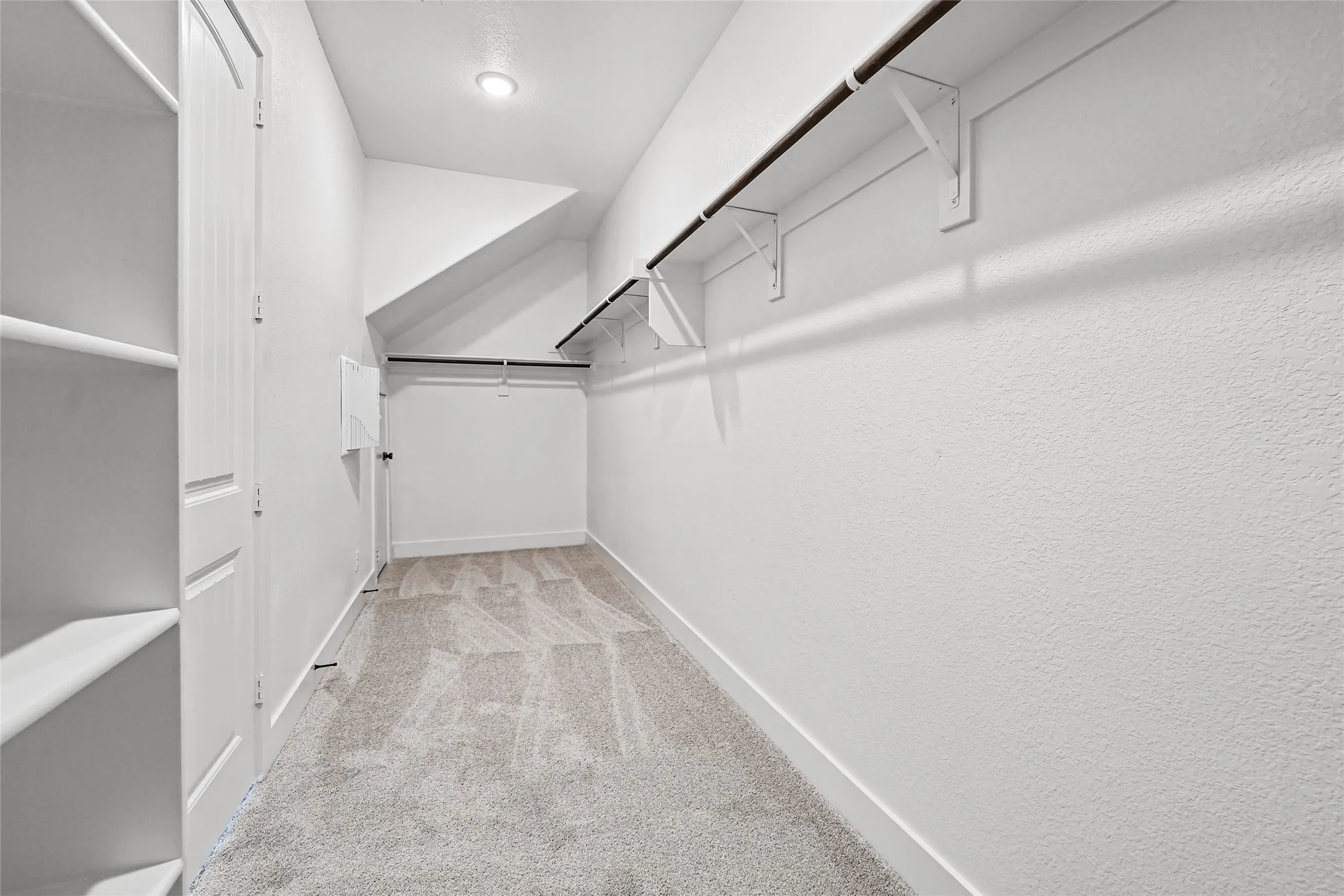 White painted walls, built-in shelving, hanging rods, recessed ceiling lighting, and carpet flooring