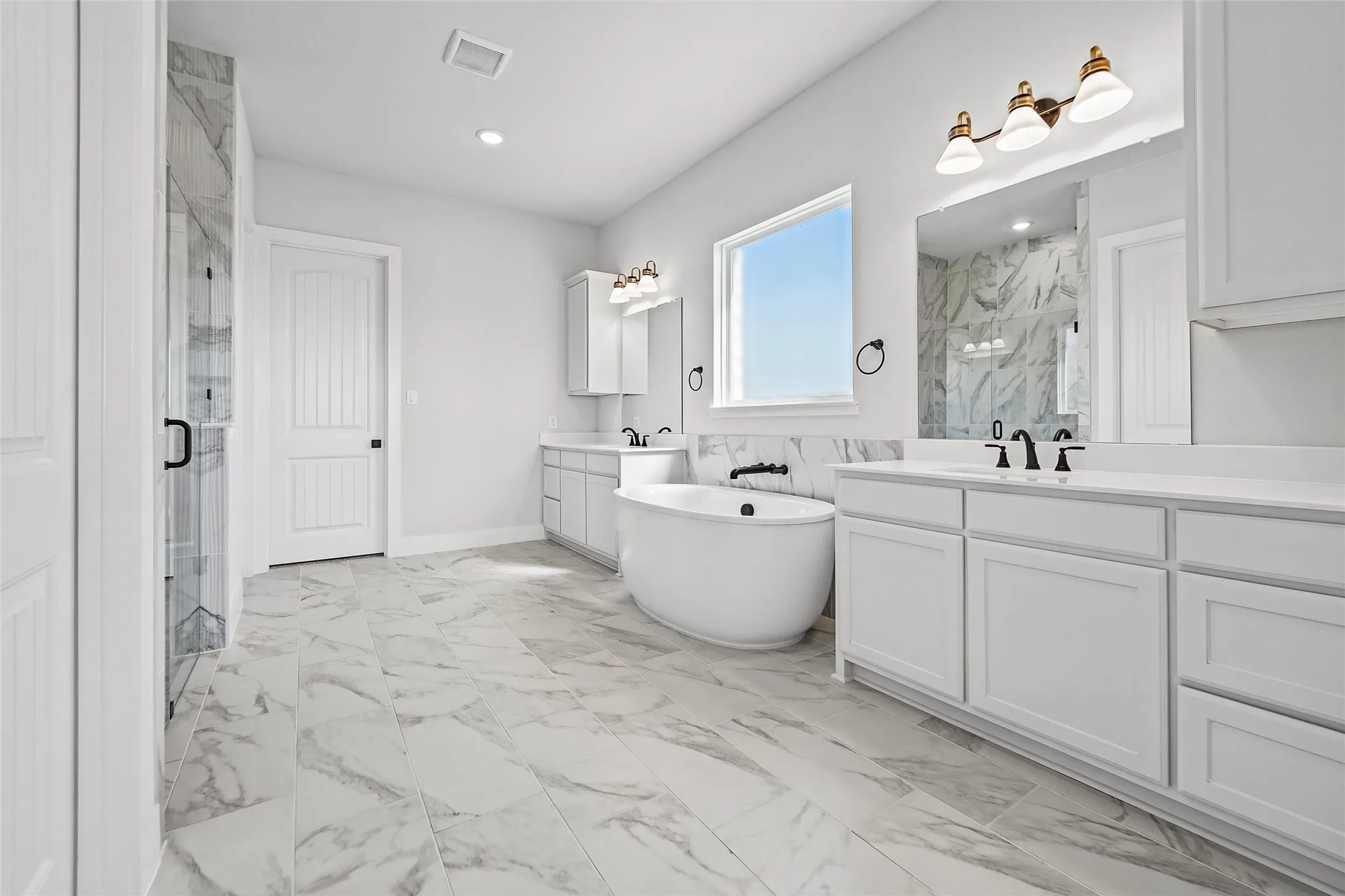 Freestanding soaking tub, dual vanity with white cabinetry, walk-in shower with glass enclosure, white tile flooring, and a large window