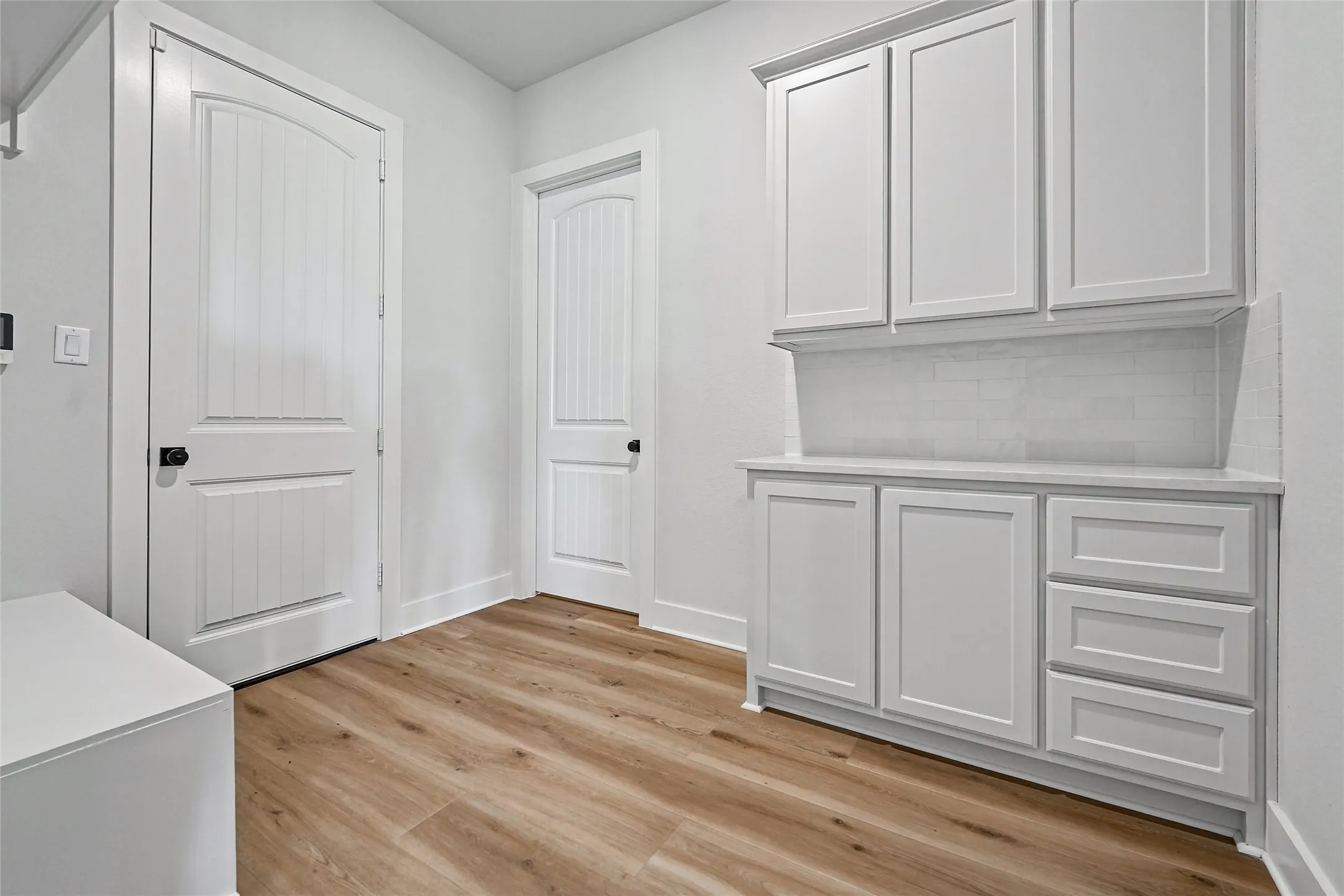 White shaker-style cabinetry with a countertop, subway tile backsplash, and wood-finish flooring