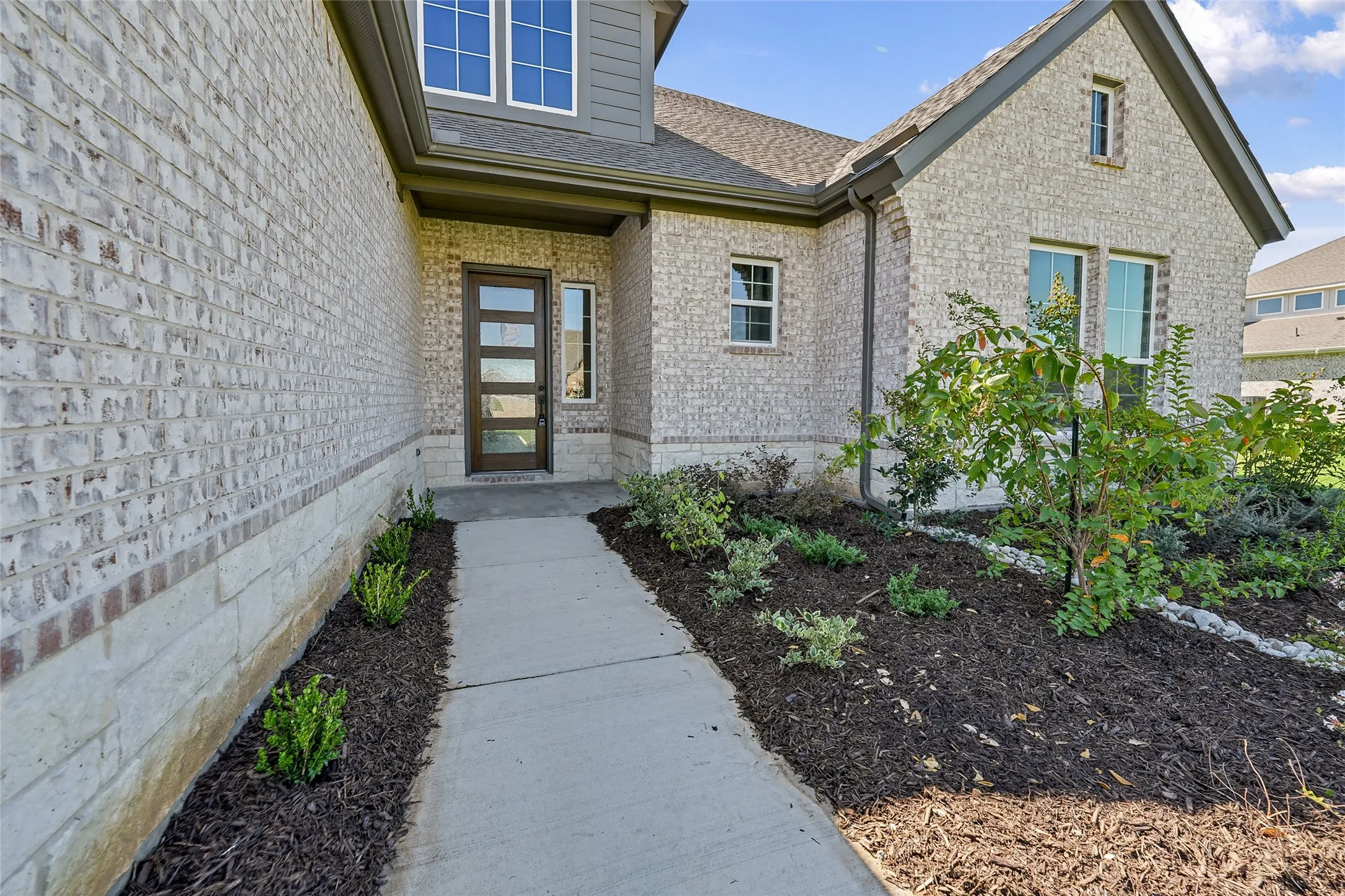 Brick exterior with stone accents, contemporary front door with vertical glass panels, and a well-maintained landscape bed with mulch