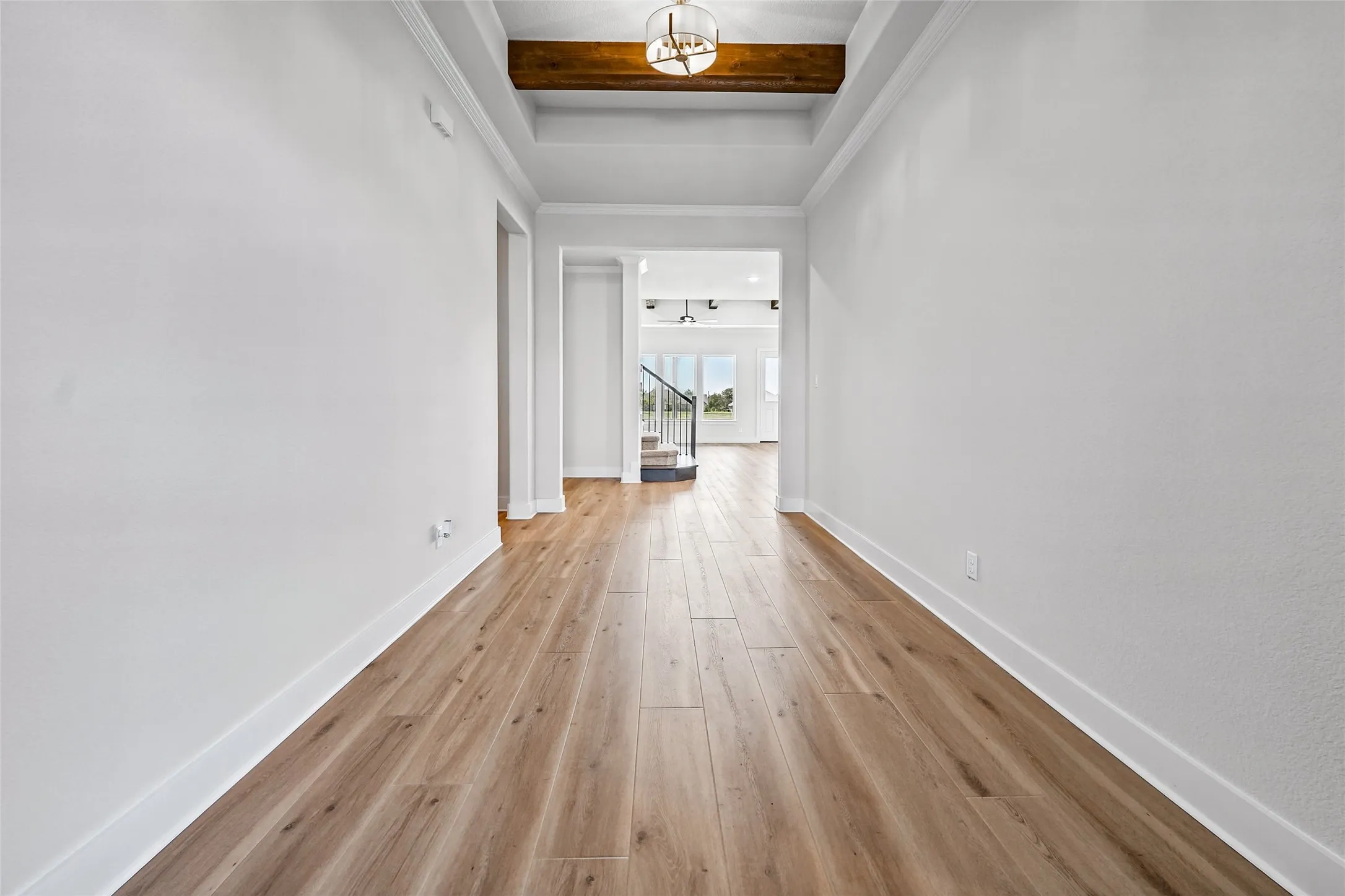 Wood-finish flooring throughout, tray ceiling with a wood beam accent, and a decorative ceiling light fixture