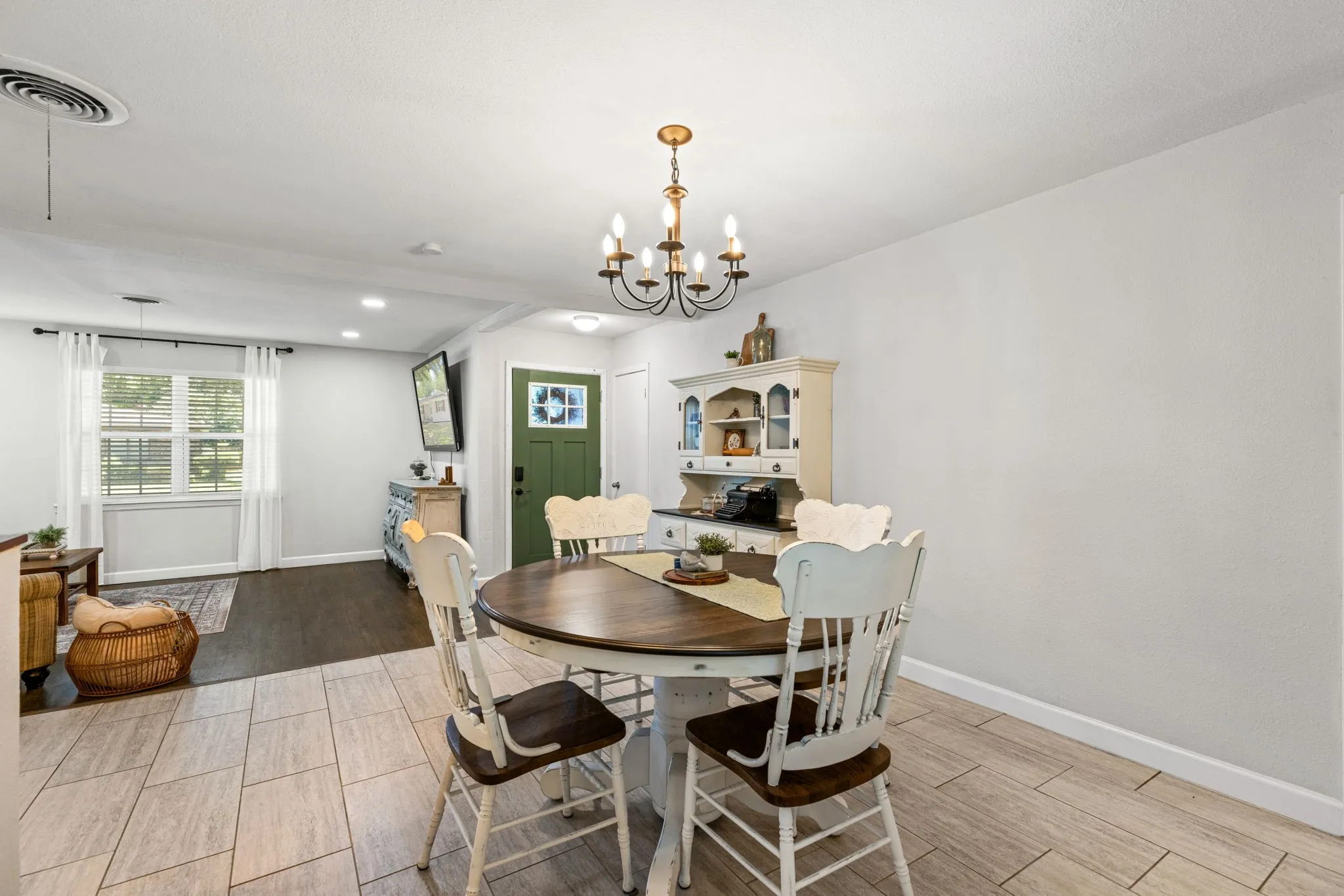 Open-concept living area featuring a prominent olive green entry door, a multi-pane window with white blinds, and two distinct flooring types: wood-finish and large format tile