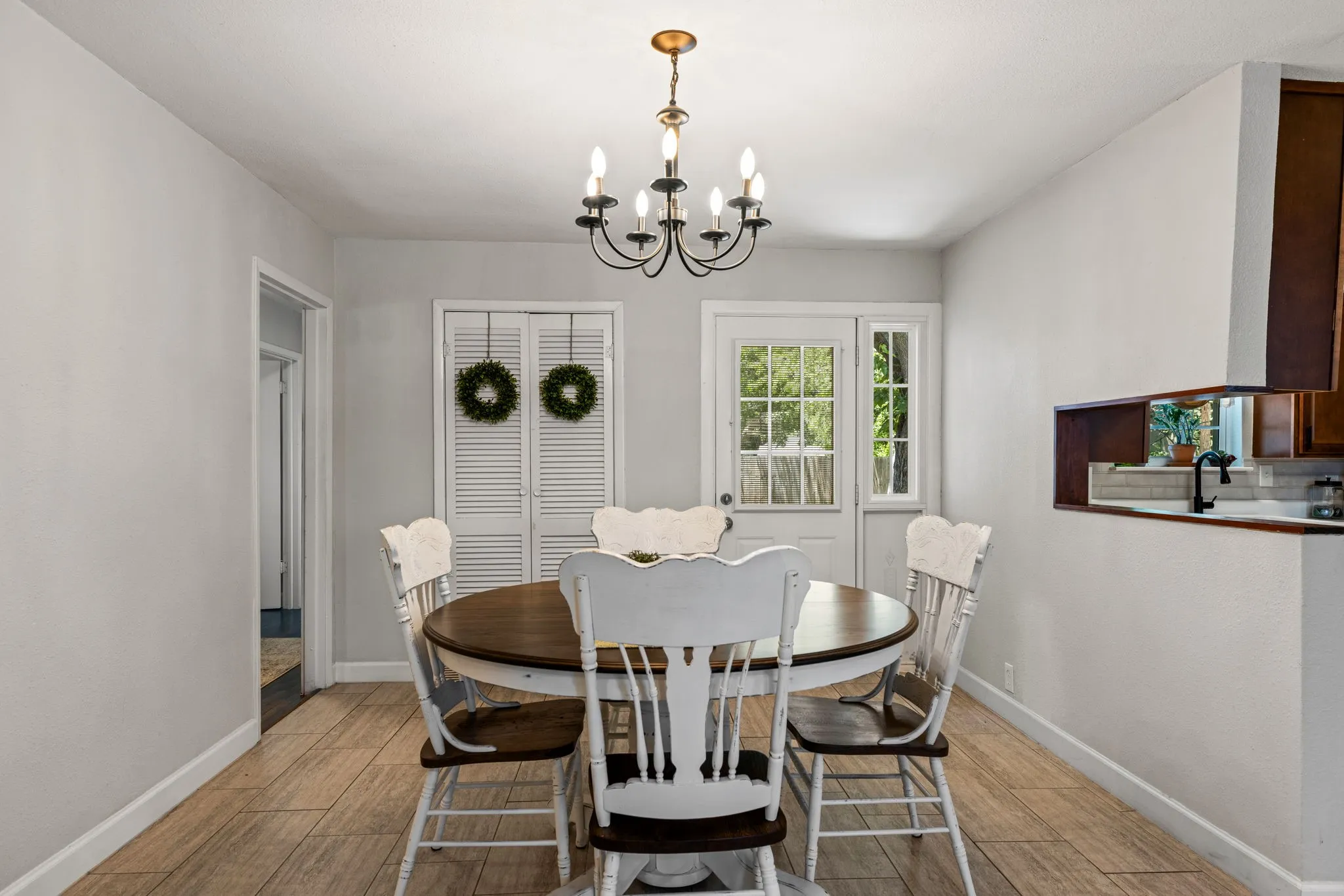 Dining area featuring wood-finish flooring, a pass-through window to the kitchen, a white paneled door, and a black chandelier