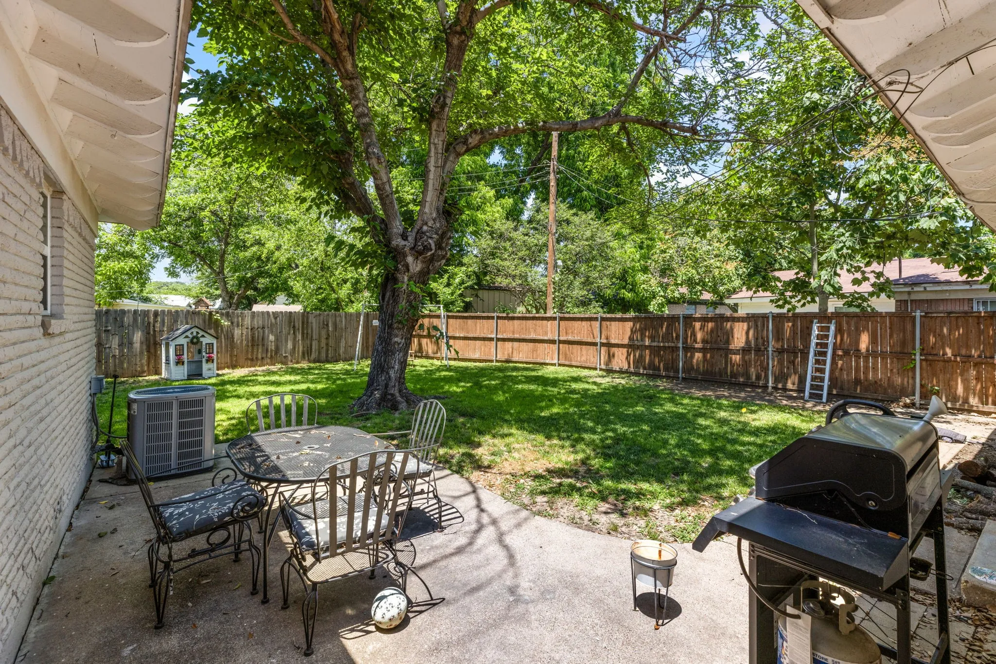 Expansive backyard featuring a mature shade tree, a concrete patio, and a wood privacy fence