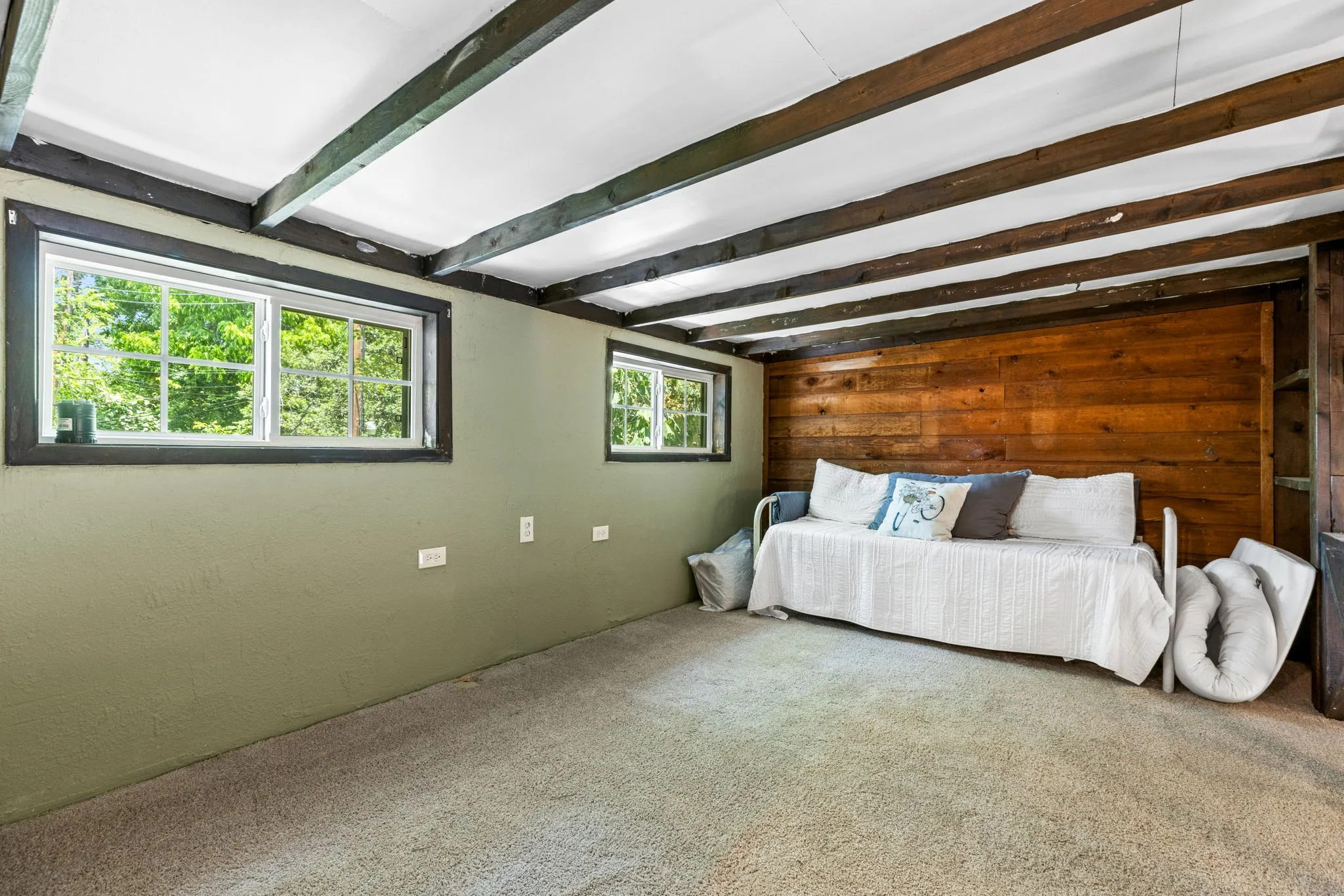 Exposed wood beam ceiling over a carpeted room featuring a wood-paneled accent wall