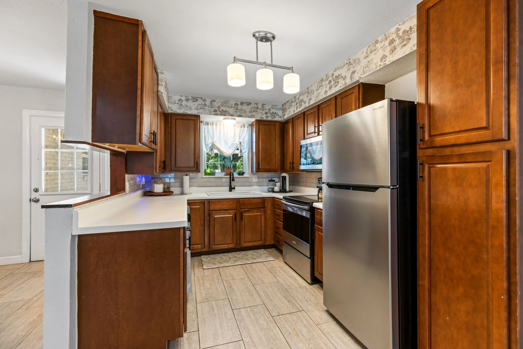 Kitchen featuring wood cabinetry, stainless steel appliances, white countertops, and light-toned tile flooring