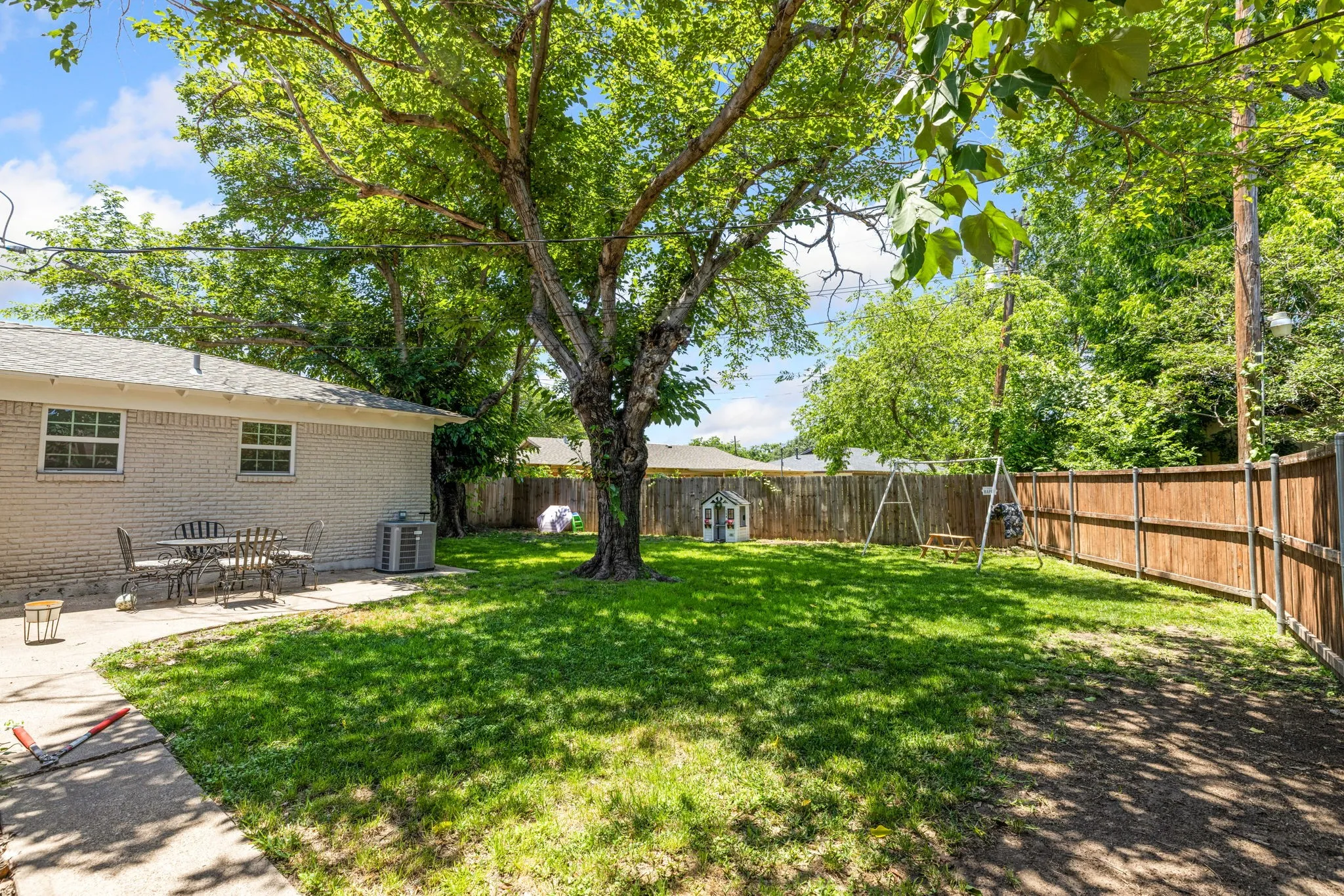 Expansive backyard featuring a mature shade tree, a manicured lawn, and a privacy fence