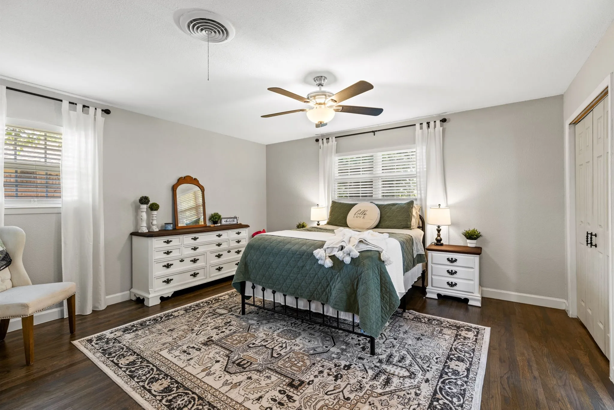 Bedroom featuring wood-finish flooring, two windows with blinds, a ceiling fan with integrated lighting, and a bi-fold closet door