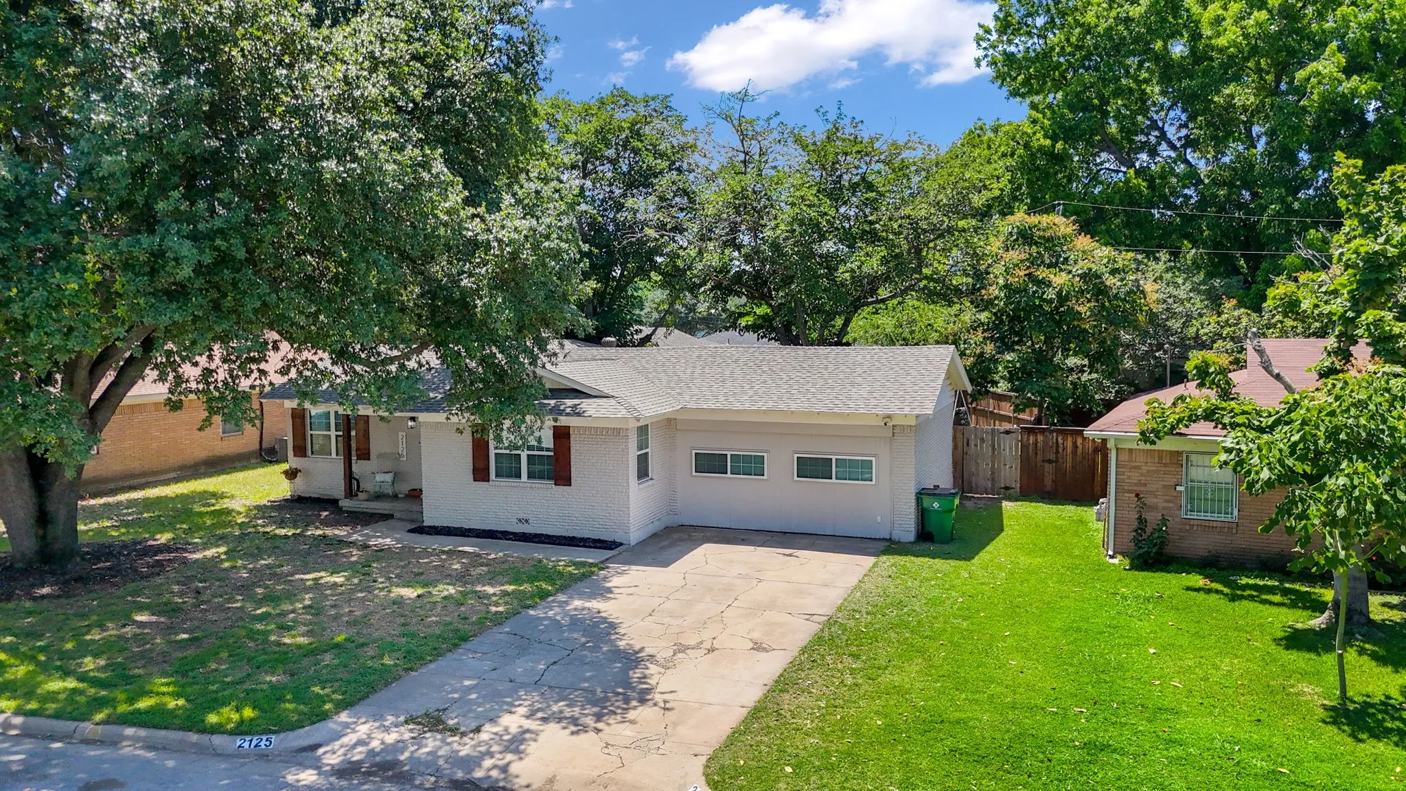Ranch-style residence featuring a light-colored exterior with dark shutters, an attached garage, and a concrete driveway
