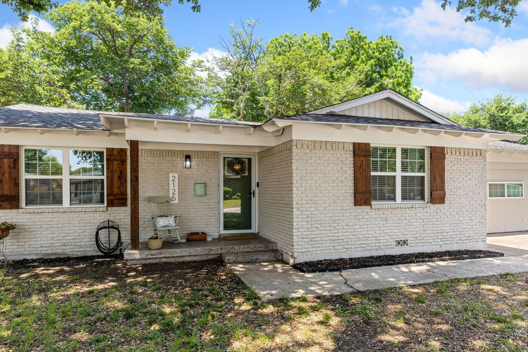 White-painted brick exterior featuring wood shutters, a covered entry, and a dark front door