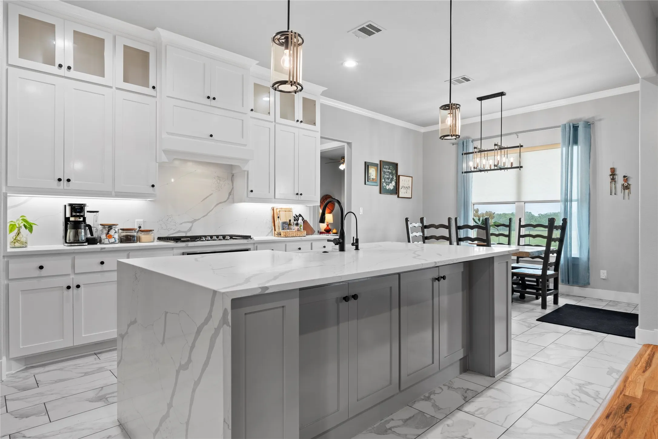 Spacious kitchen featuring an expansive island with a waterfall countertop, white shaker-style cabinetry, and a matching stone backsplash