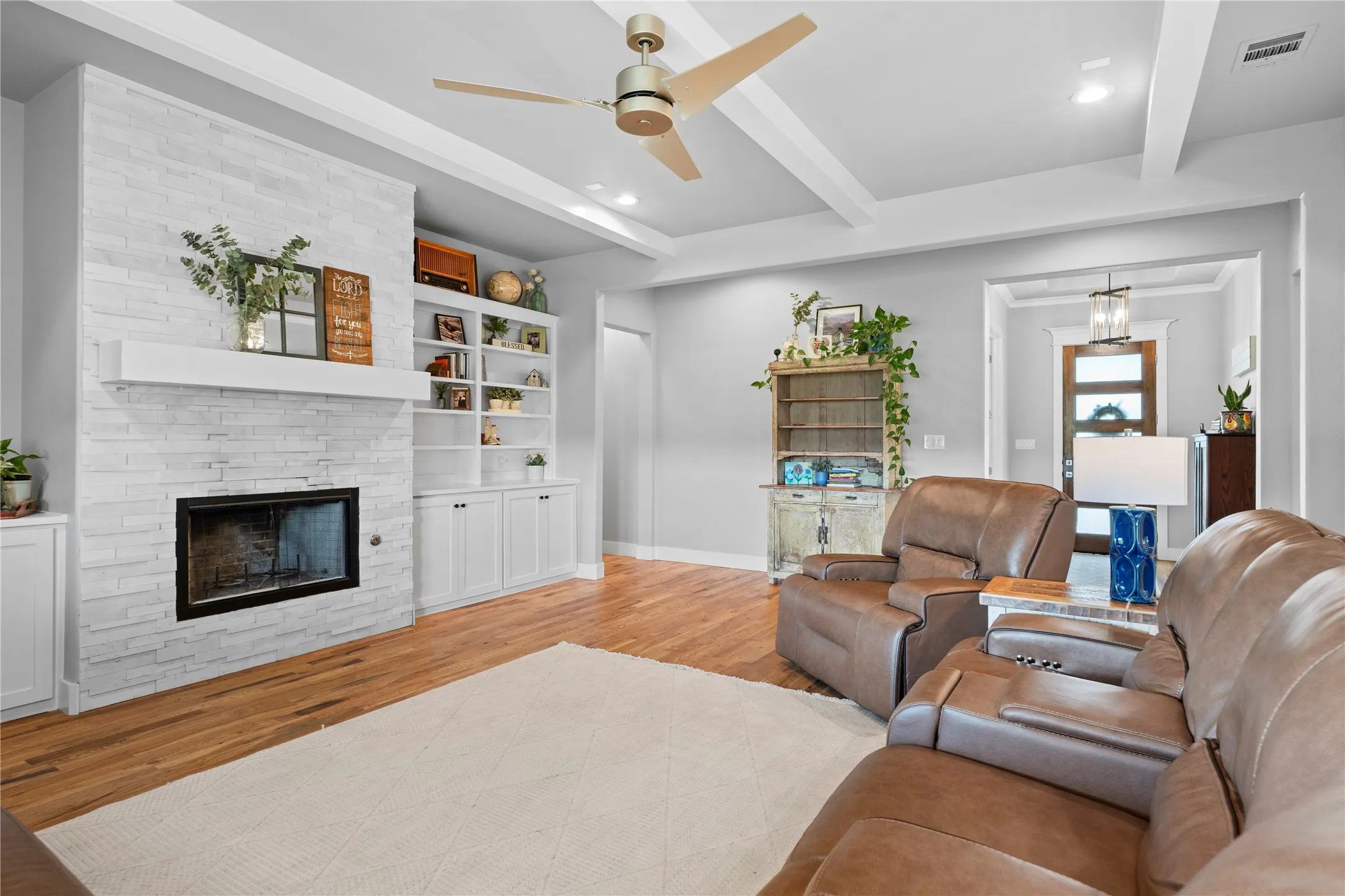 Living area featuring a textured white brick fireplace with a mantle, built-in shelving and cabinetry, wood-finish flooring, and a ceiling fan