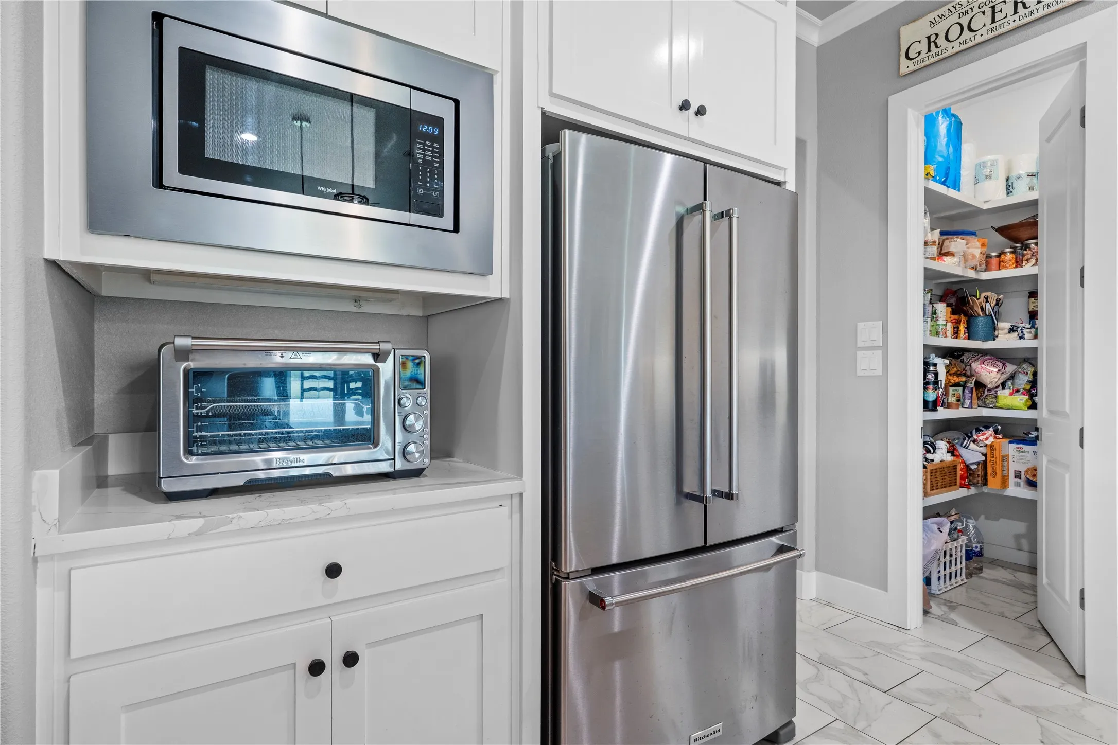 Stainless steel appliances, including a built-in microwave and French door refrigerator, complement white cabinetry