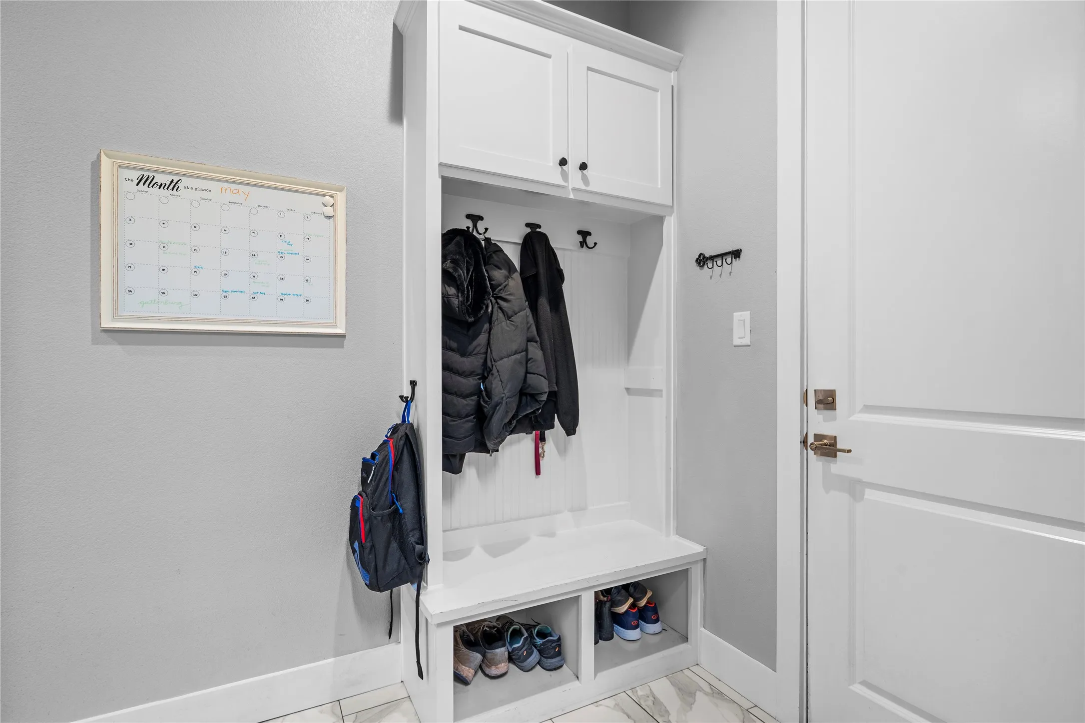 Built-in white mudroom cabinetry featuring upper storage, coat hooks, a bench, and lower shoe cubbies