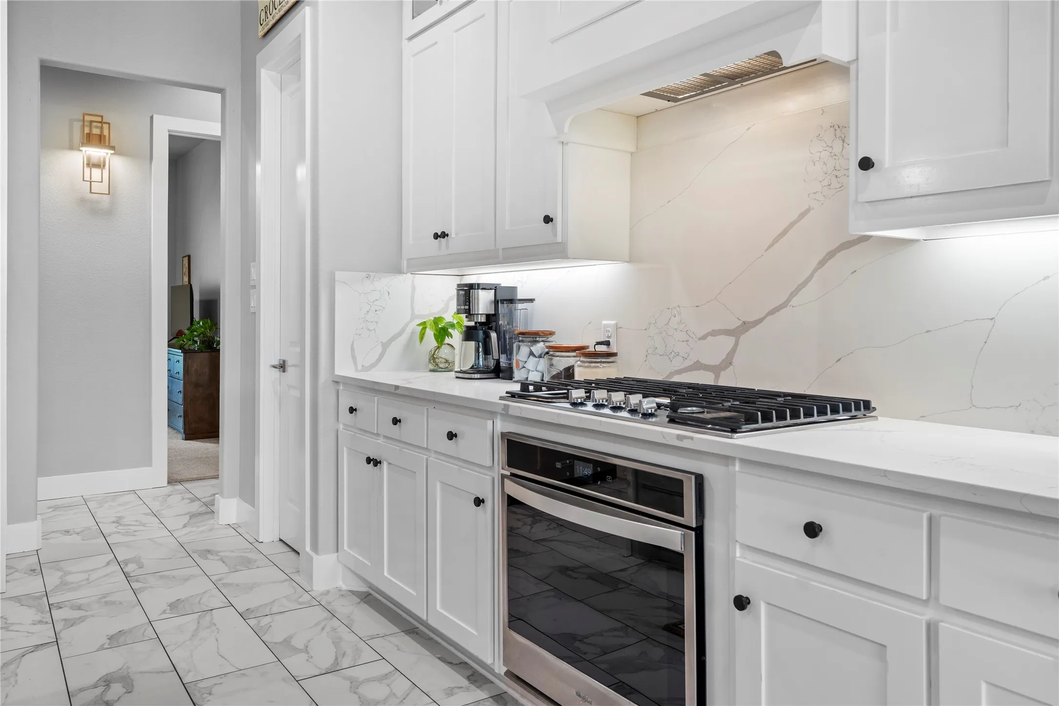 Gourmet kitchen featuring a stainless steel gas cooktop and oven, white cabinetry with black hardware, under-cabinet lighting, and a patterned backsplash extending to the countertop
