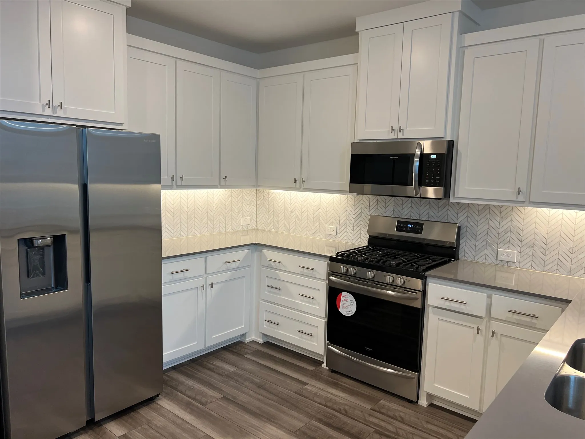 Kitchen featuring stainless steel appliances, white cabinets, tasteful backsplash, and dark wood-type flooring