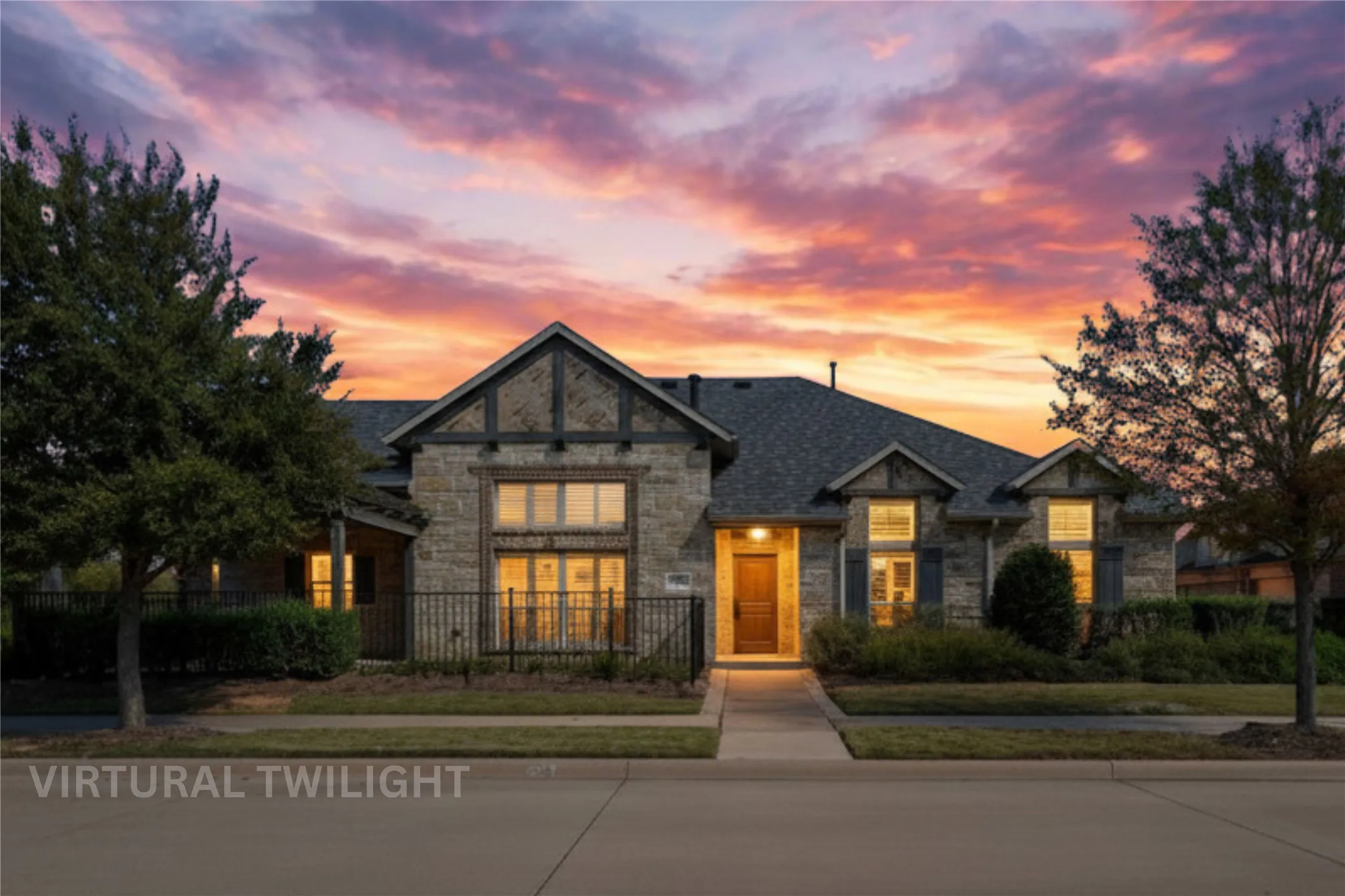 Stone and brick facade residence featuring a prominent gabled entry, dark shingle roof, decorative shutters, and mature front landscaping
