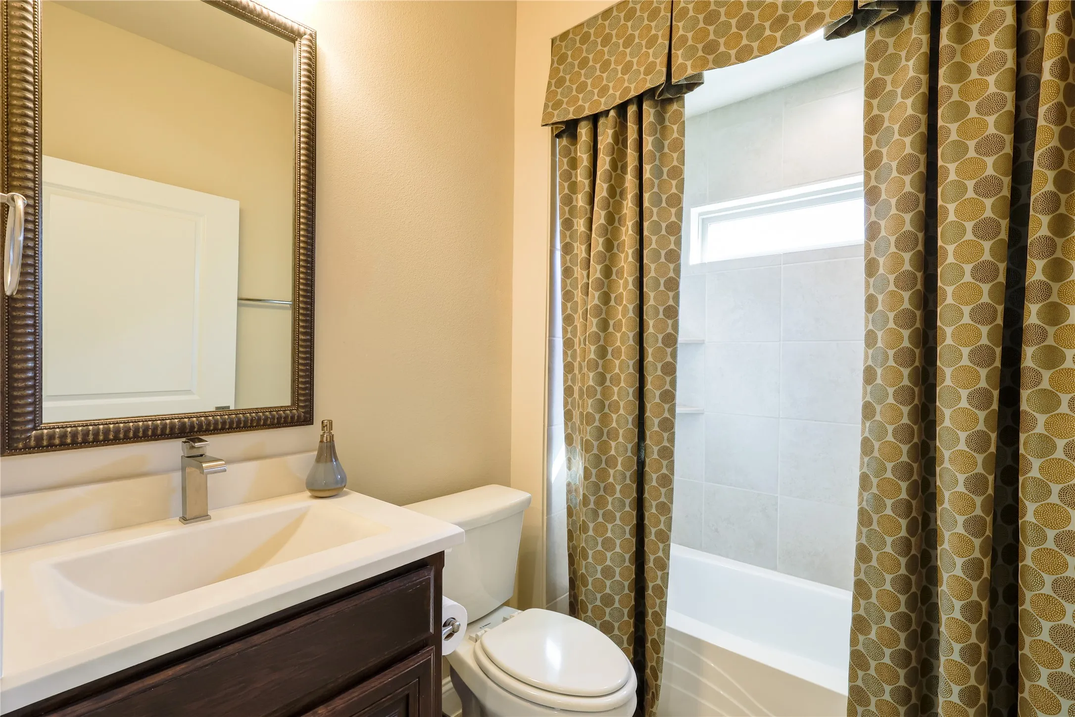 Bathroom featuring a dark wood-finish vanity, white countertop with integrated sink, brushed nickel faucet, and a large decorative framed mirror