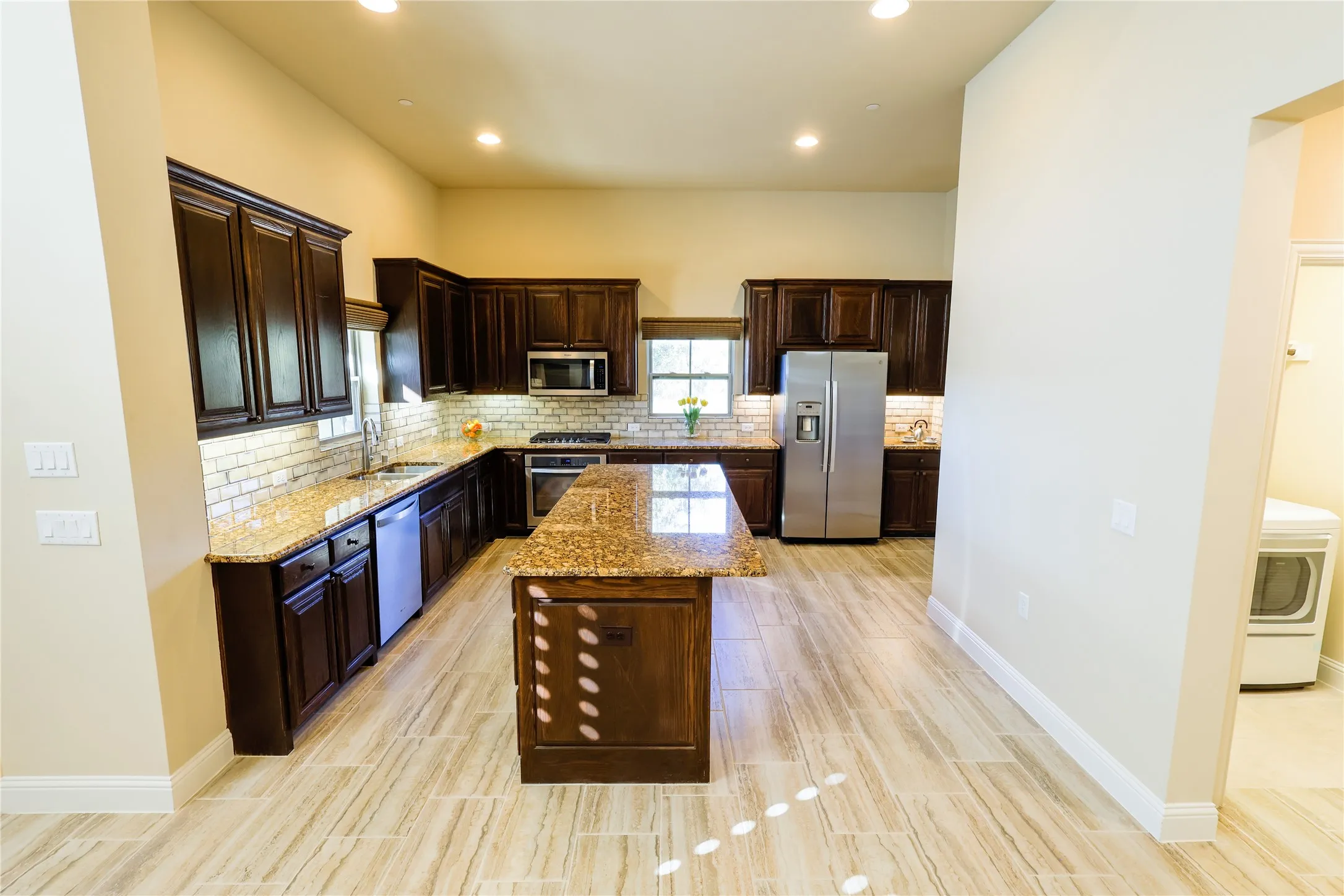 Open-concept kitchen featuring dark wood cabinetry, granite countertops, a matching kitchen island, stainless steel appliances, and wood-finish tile​​‌​​​​‌​​‌‌​‌‌​​​‌‌​‌​‌​‌​​​‌​​ flooring