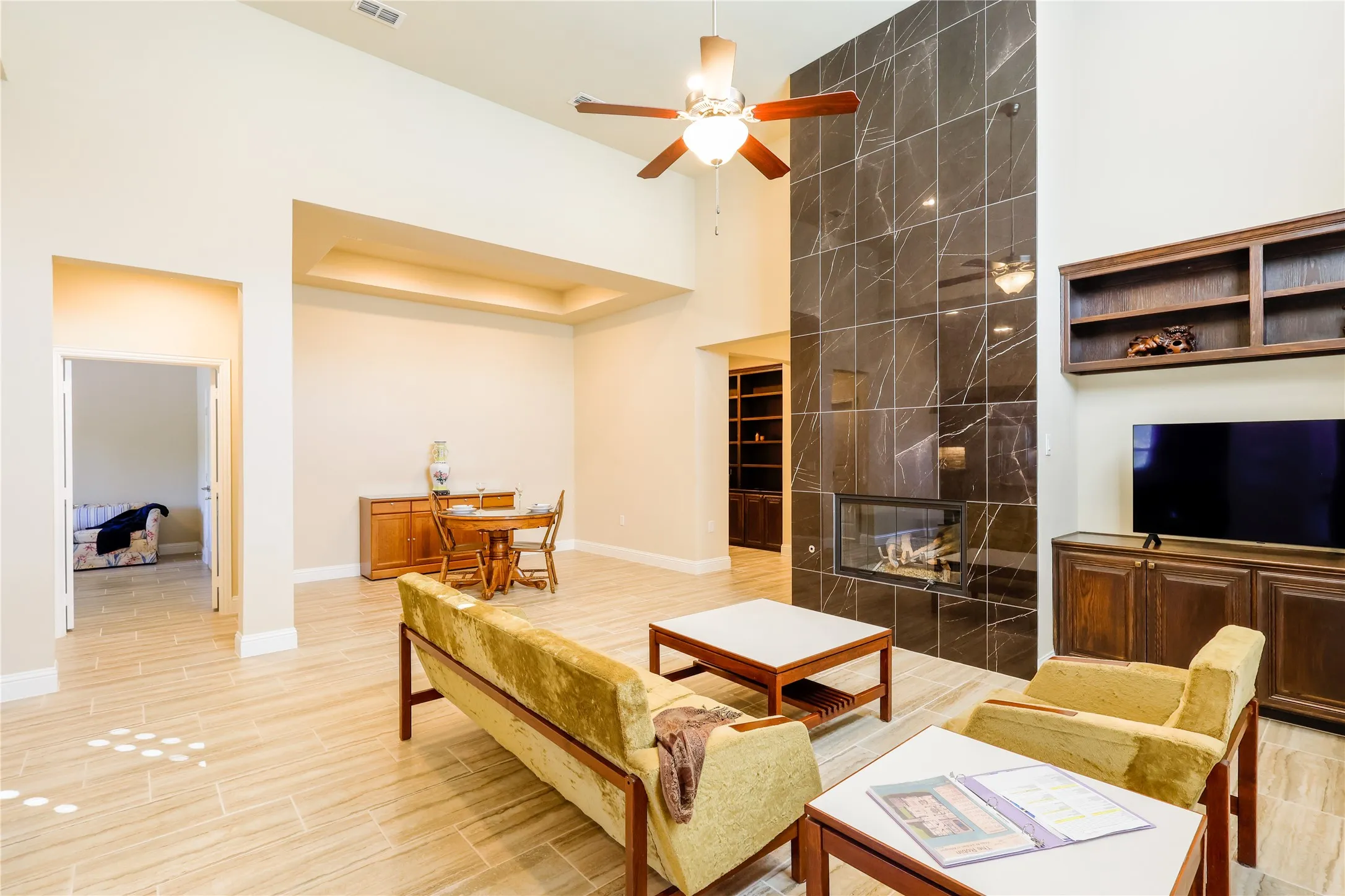 Living area featuring a floor-to-ceiling dark tiled fireplace with a built-in linear electric fireplace, high ceilings, wood-finish flooring, and a ceiling fan