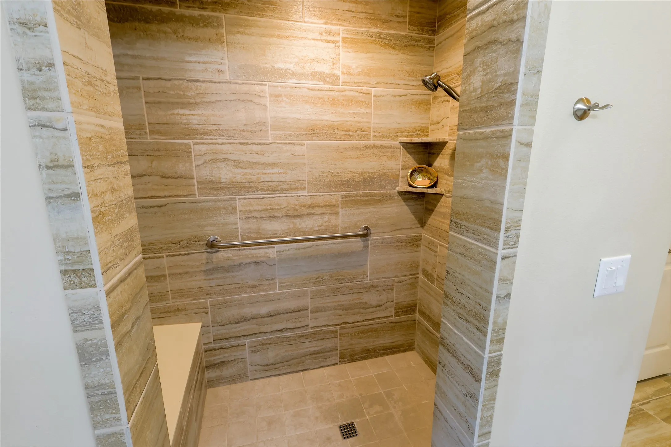 Walk-in shower with large-format stone-look wall tiles, coordinating floor tiles, and a built-in corner shelf