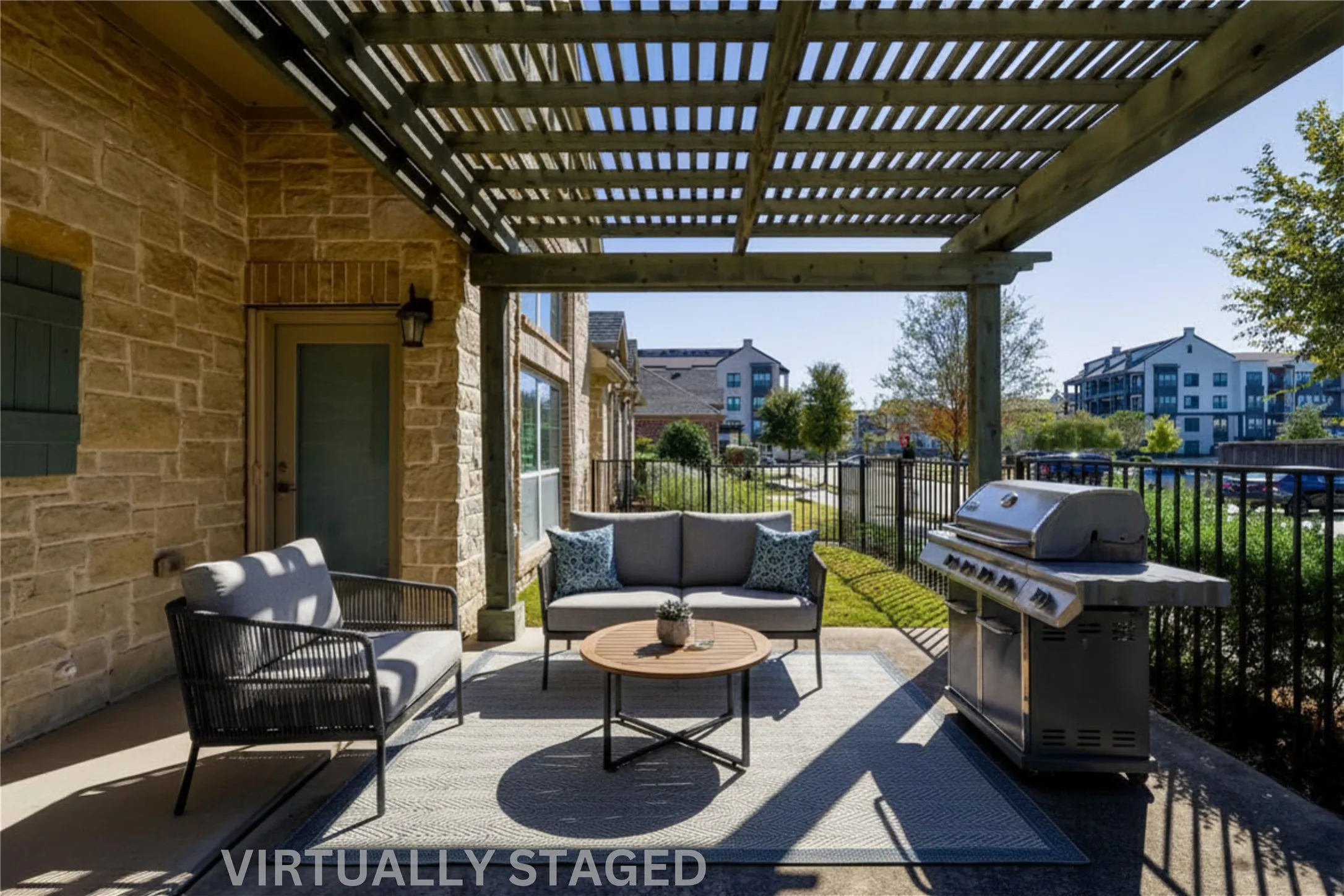 Outdoor patio featuring a wooden pergola, stone-clad exterior wall, and a black wrought iron fence