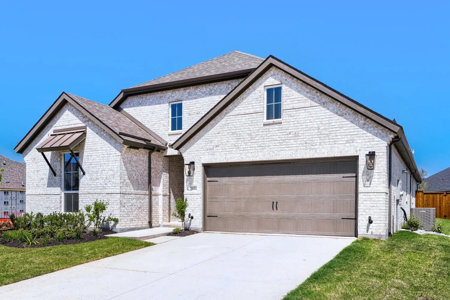 White brick exterior, gabled roofline, metal awning, wood-finish garage door, and exterior lighting fixtures