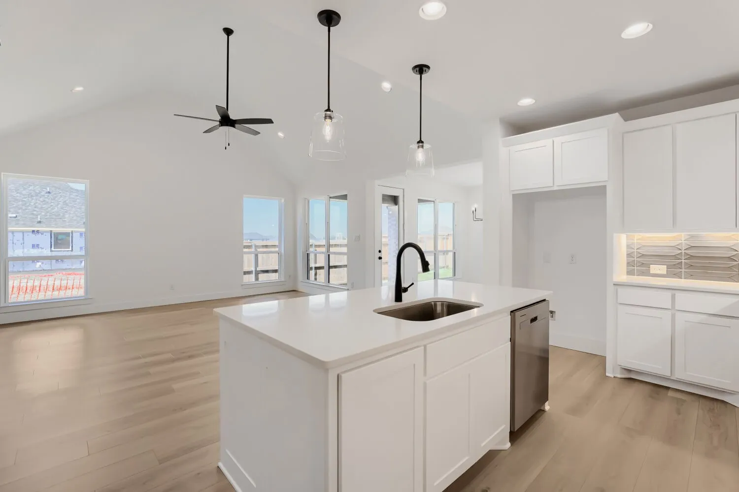 Vaulted ceilings, wood-finish flooring, white cabinetry, island with sink and stainless steel dishwasher, and recessed lighting