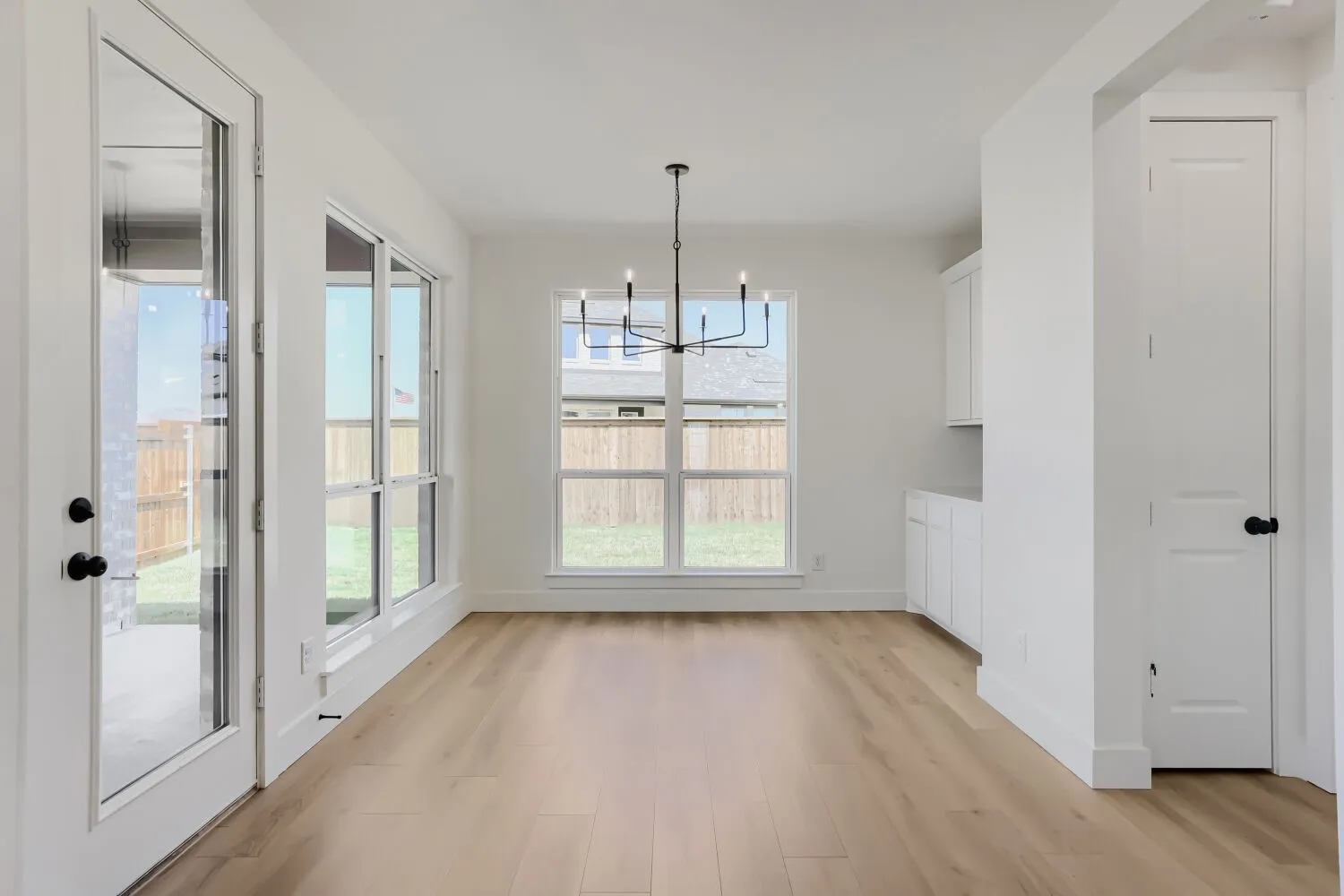 Light wood-finish flooring, white walls, and a modern black chandelier