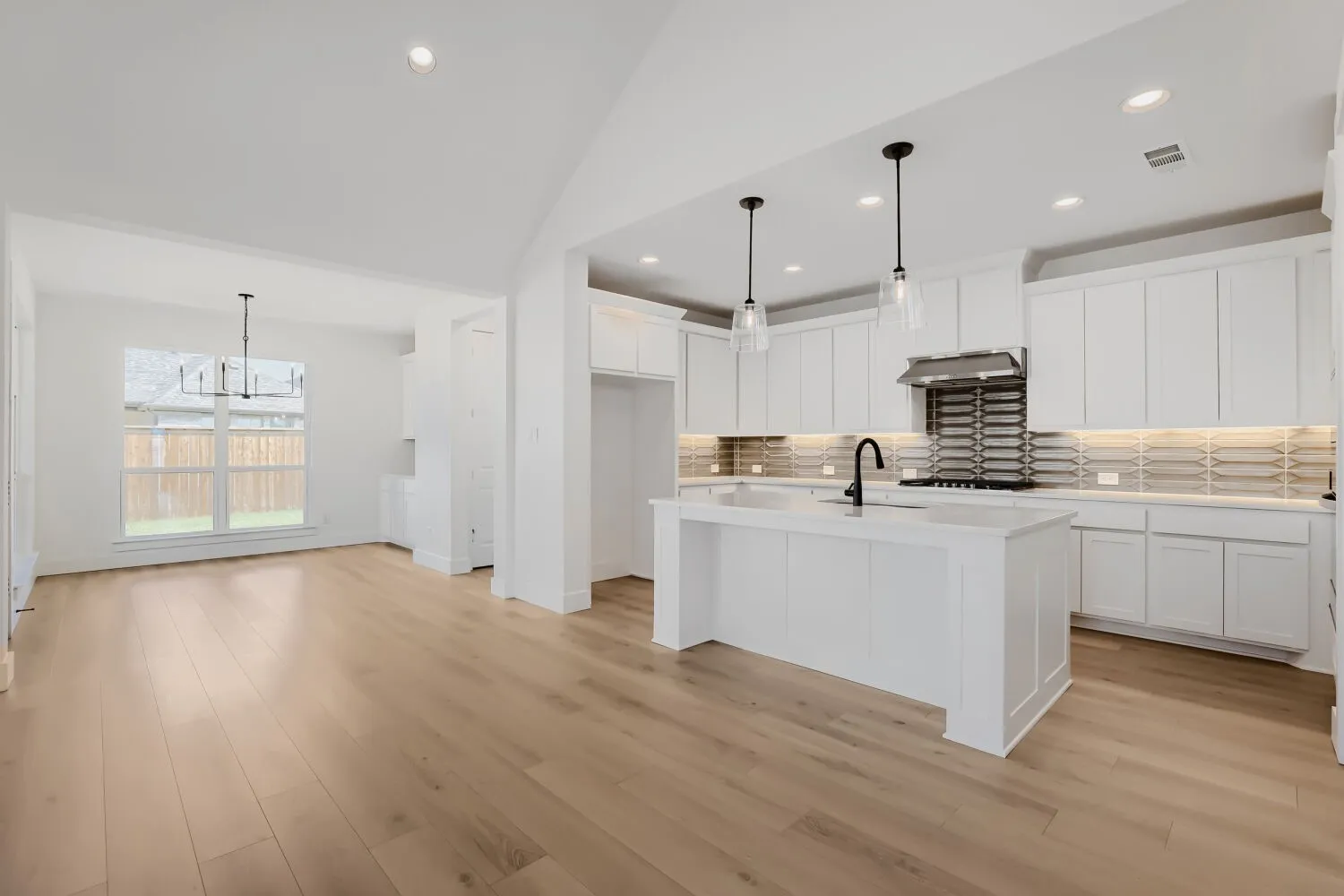 Open-concept living space featuring wood-finish flooring, a vaulted ceiling, and a kitchen with white cabinetry, a central island, and pendant lighting