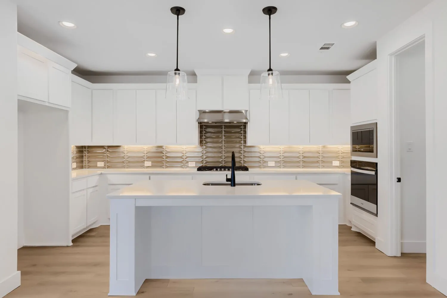 White cabinetry, stainless steel appliances, recessed lighting, wood-finish flooring, and a central island with pendant lighting