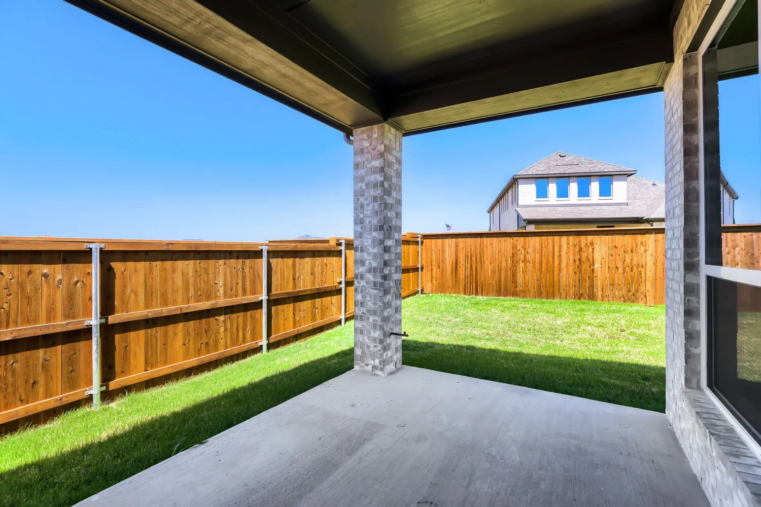 Covered patio with a concrete slab, supporting brick column, and an expansive grassy area