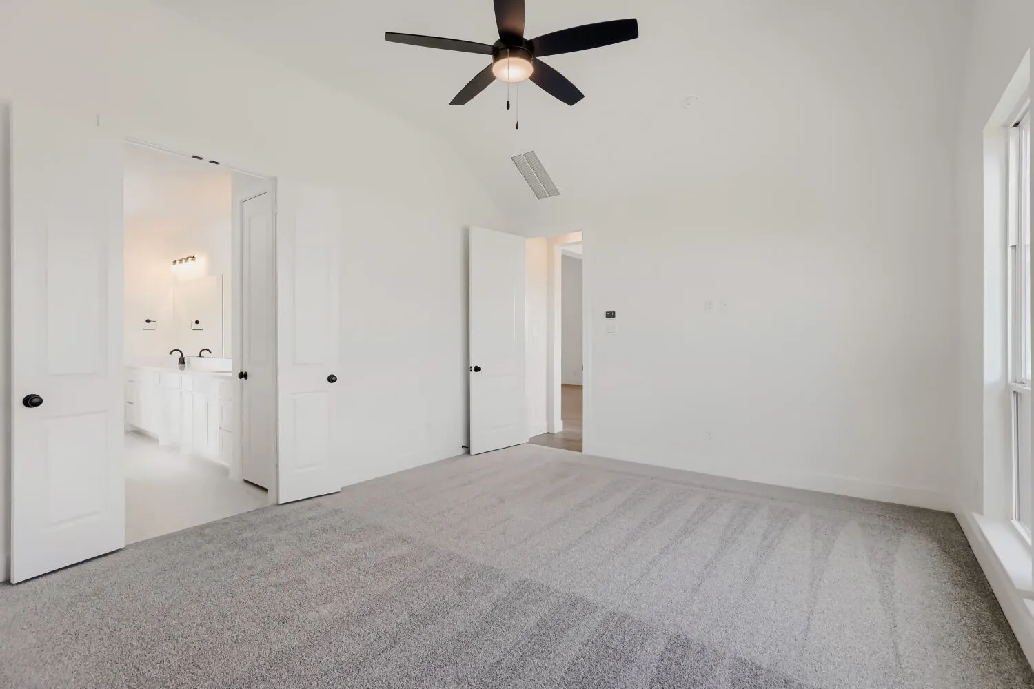 White interior walls, vaulted ceiling, ceiling fan with light fixture, light gray carpet, and white-framed window