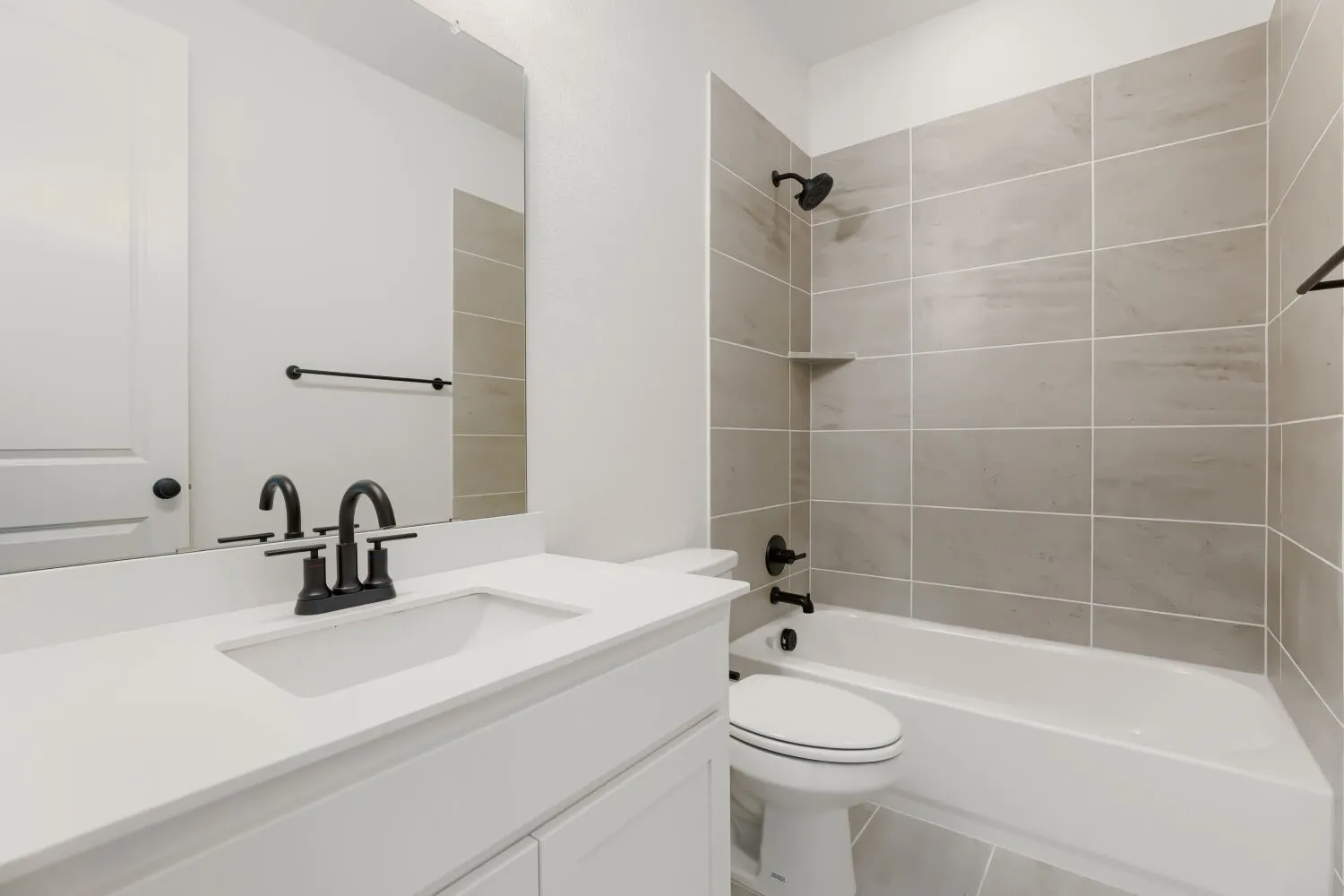 Contemporary bath featuring a white vanity with integrated sink, matte black fixtures, and a tiled shower-over-tub with an integrated shelf