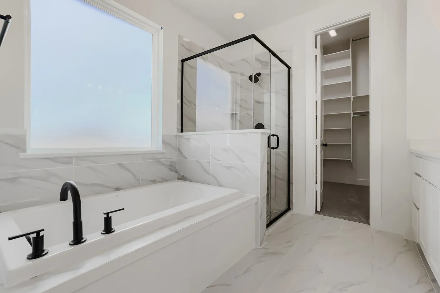 White soaking tub with matte black fixtures, glass-enclosed shower with black trim, and tile flooring