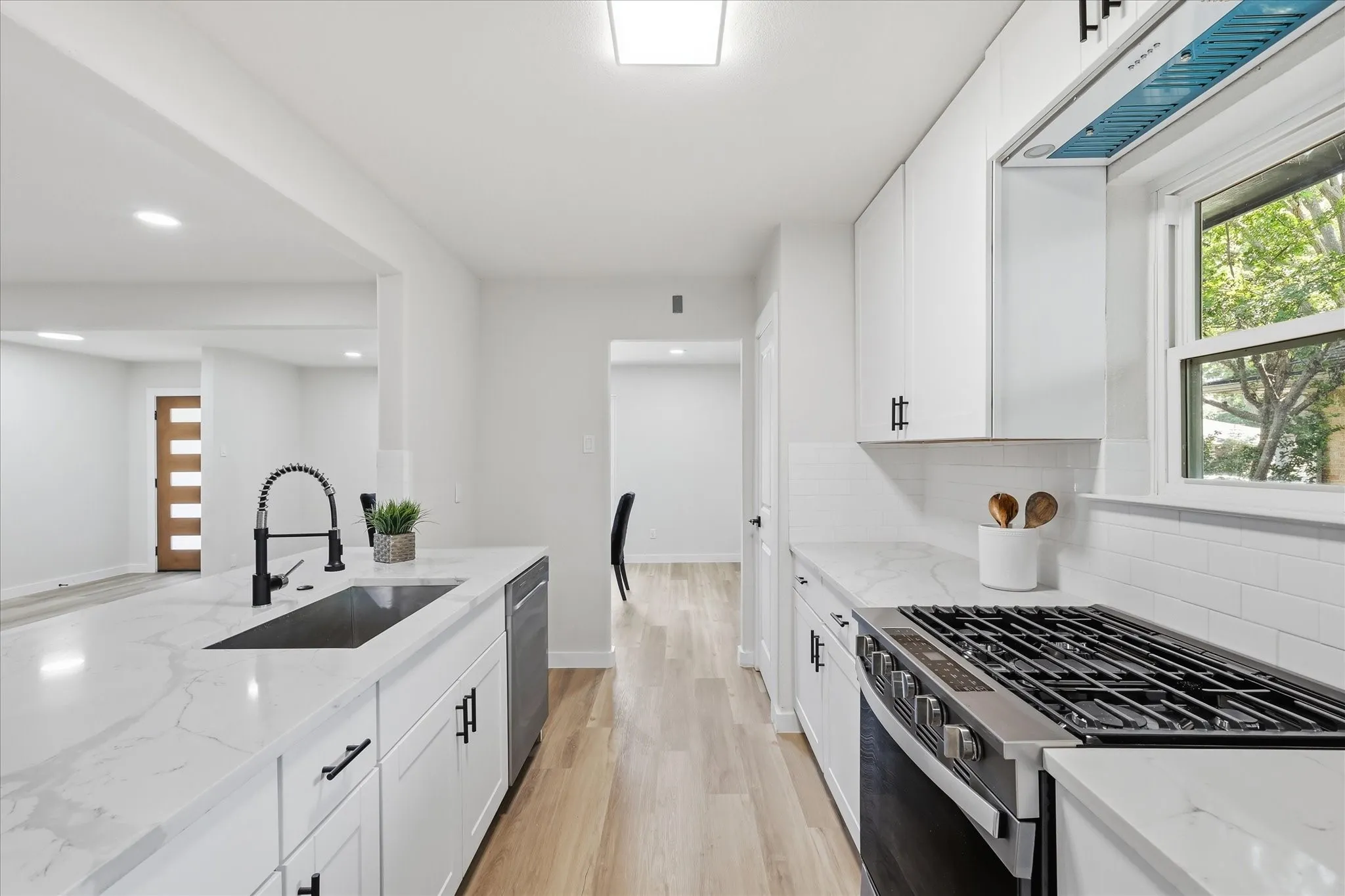 Modern kitchen featuring white cabinetry with matte black hardware, light wood-finish flooring, and white countertops