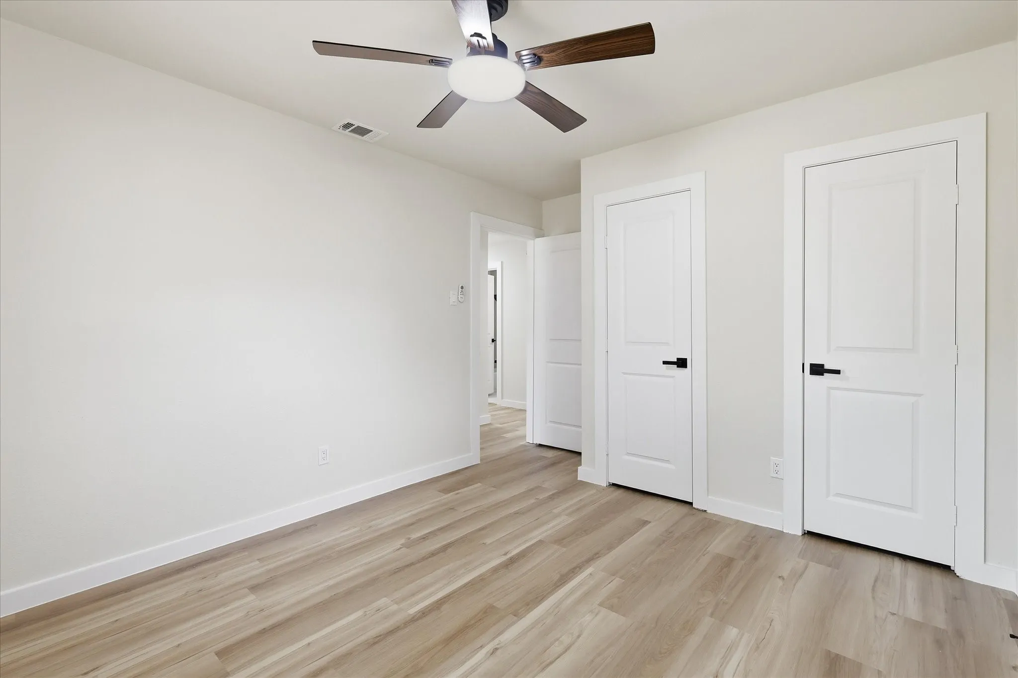 Interior room featuring wood-finish flooring, white walls, and a contemporary ceiling fan with dark wood-look blades