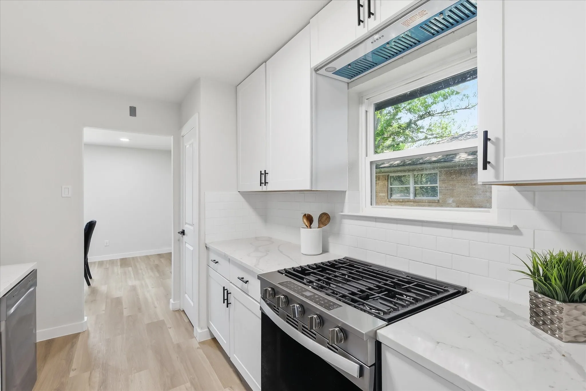 Kitchen featuring white shaker cabinetry, stainless steel range, white subway tile backsplash, light-toned wood-finish flooring, and solid surface countertops