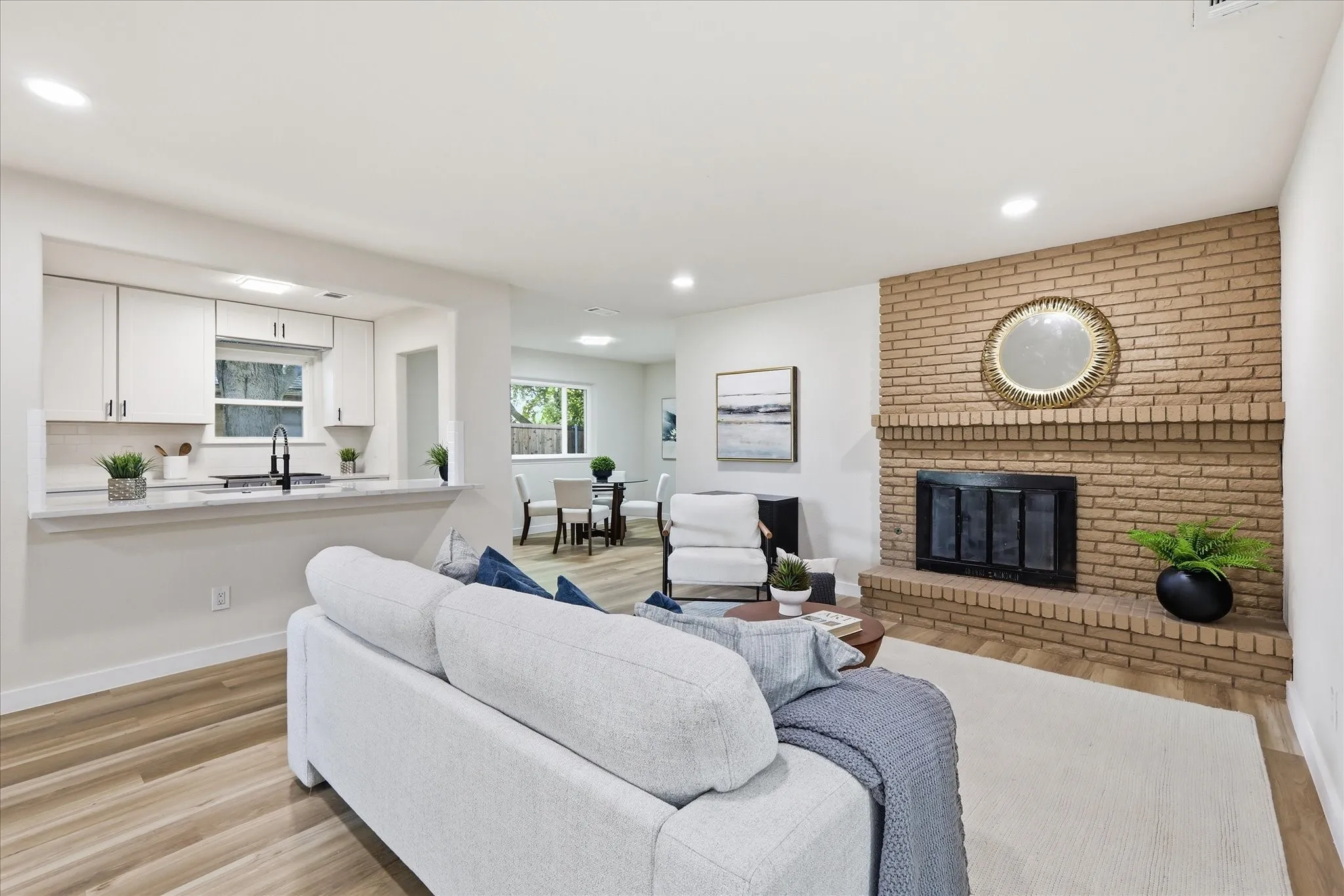 Living area featuring a brick fireplace, wood-finish flooring, recessed lighting, and a partial view of the kitchen with light cabinetry and a breakfast bar