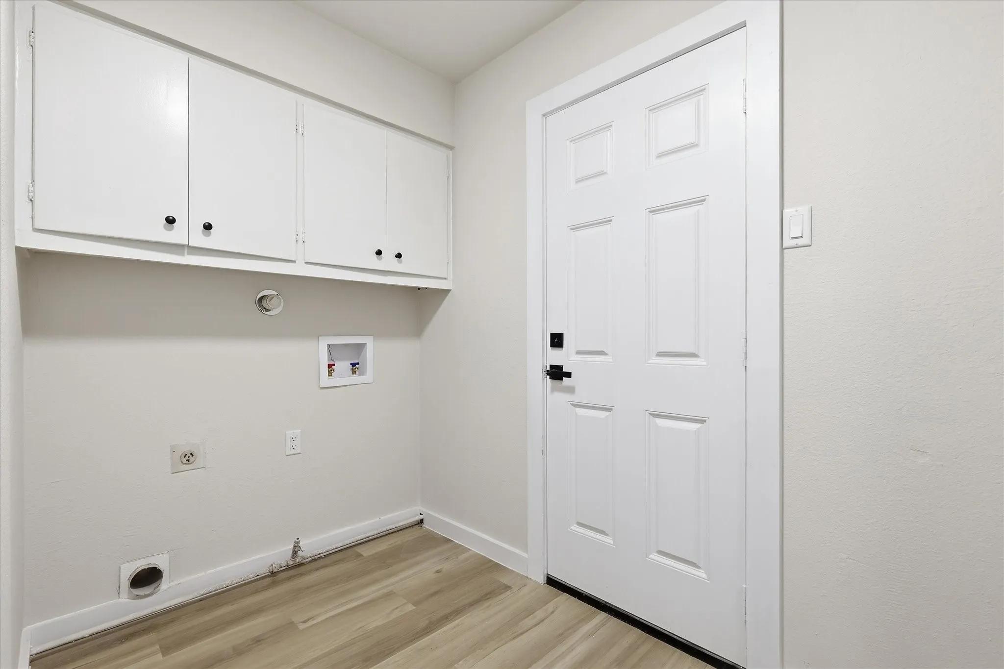 Utility room featuring white shaker-style cabinetry, wood-finish flooring, a six-panel door with black hardware, and light neutral wall paint