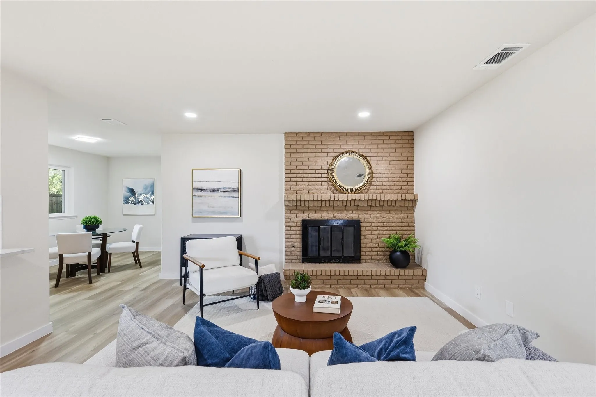 Living area featuring a brick fireplace with a black firebox, light wood-finish flooring, recessed lighting, and white walls