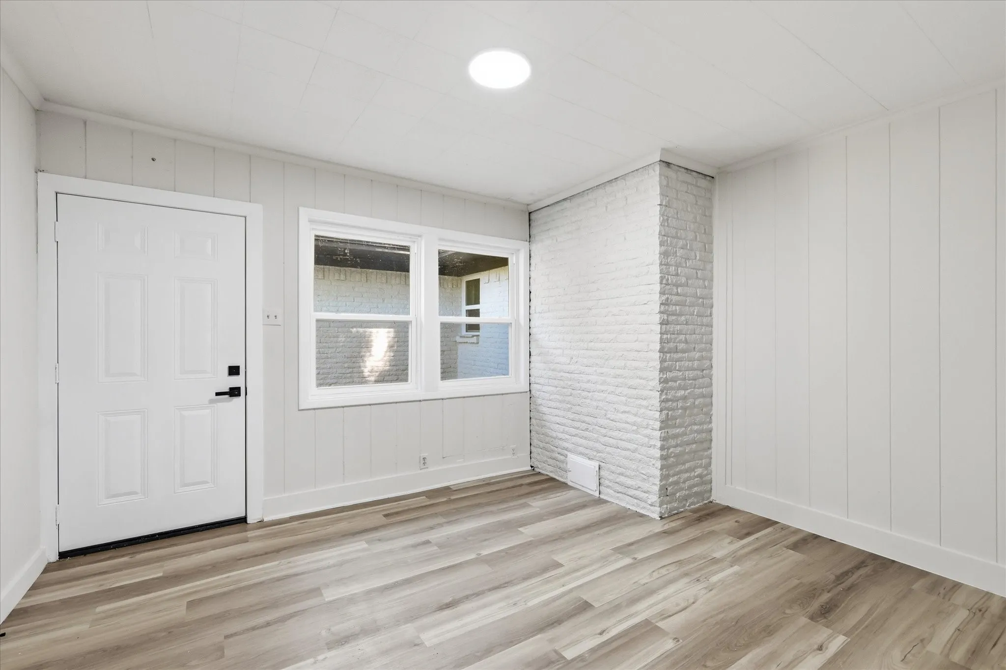 Interior room featuring light wood-finish flooring, white paneled walls, and a white painted brick column