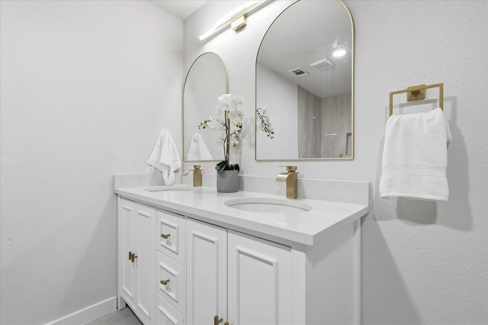 Dual vanity with white cabinetry, integrated sinks, quartz countertops, and gold-finish hardware