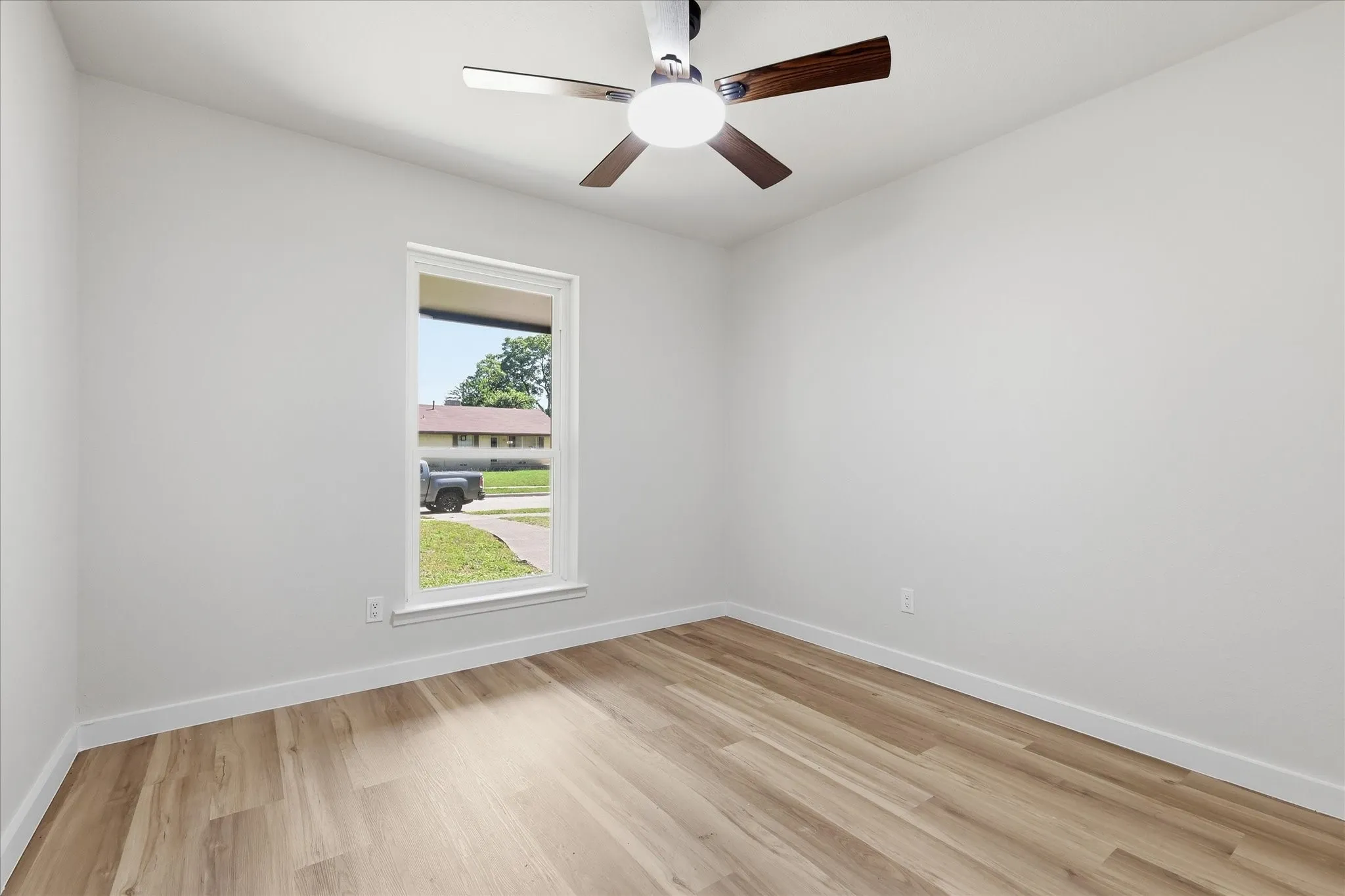 Room featuring light wood-finish flooring, white baseboards, a single window with white trim, and a ceiling fan with brushed nickel and wood-finish blades